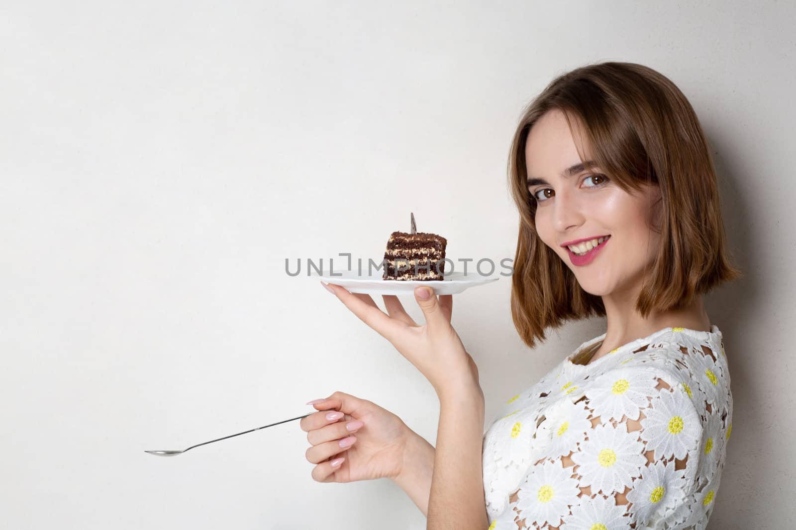 Merry brunette woman holding tasty cake over a grey background. Empty space
