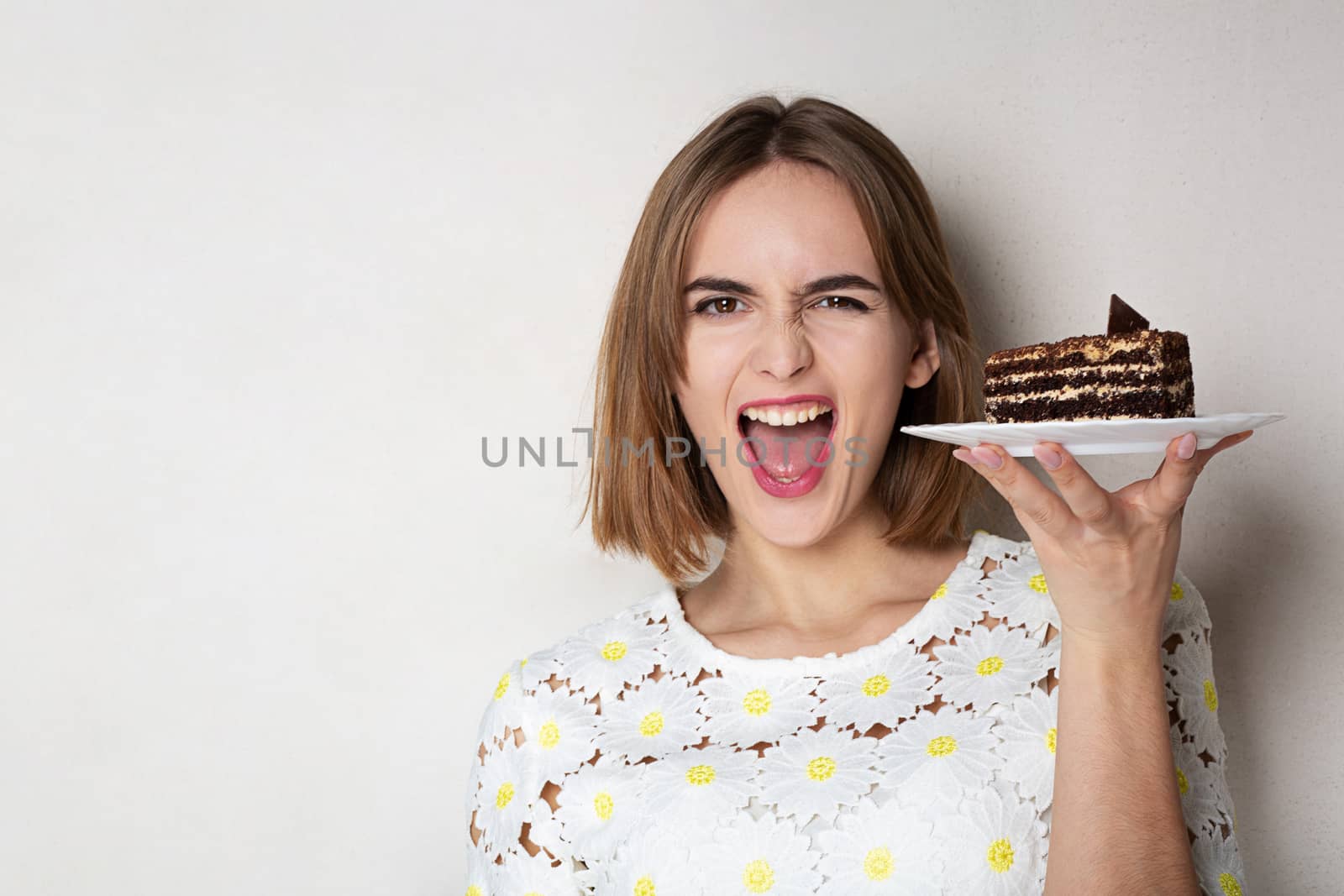 Happy excited woman holding a plate with tasty chocolate cake over a grey background. Empty space