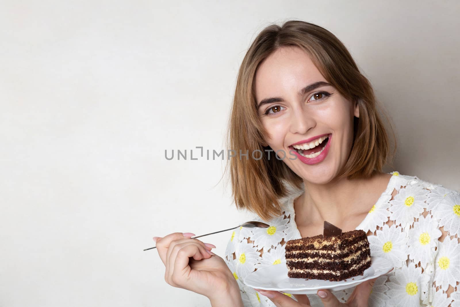 Cheerful woman holding a plate with tasty chocolate cake over a grey background. Empty space