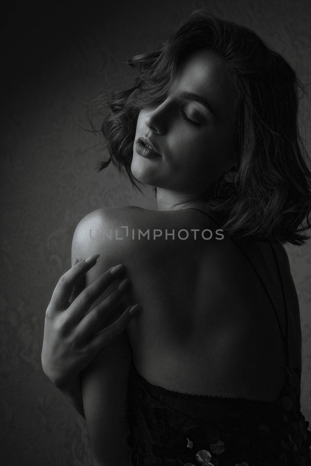 Glorious brunette woman posing in dark studio with closed eyes. Monochrome color