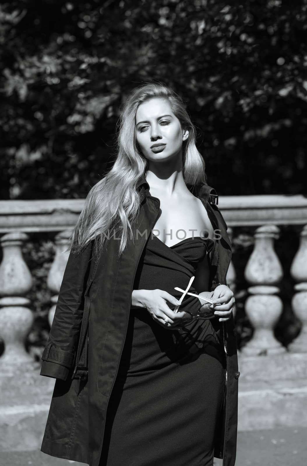 Outdoor shot of wonderful woman with long hair wearing dress and black autumn coat. Monochrome