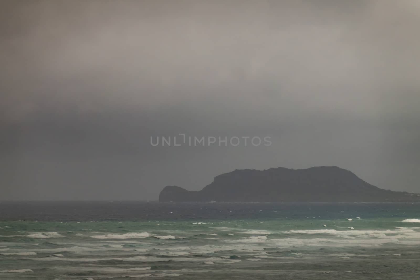 Mokolii island under rainy clouds off east coast, Oahu, Hawaii,  by Claudine