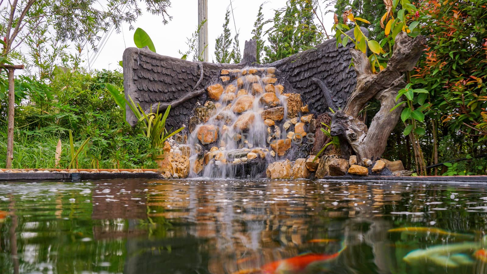 Fish pond with waterfall fountain. Garden waterfall landscaping with fishes, rocks, flowers and plants.