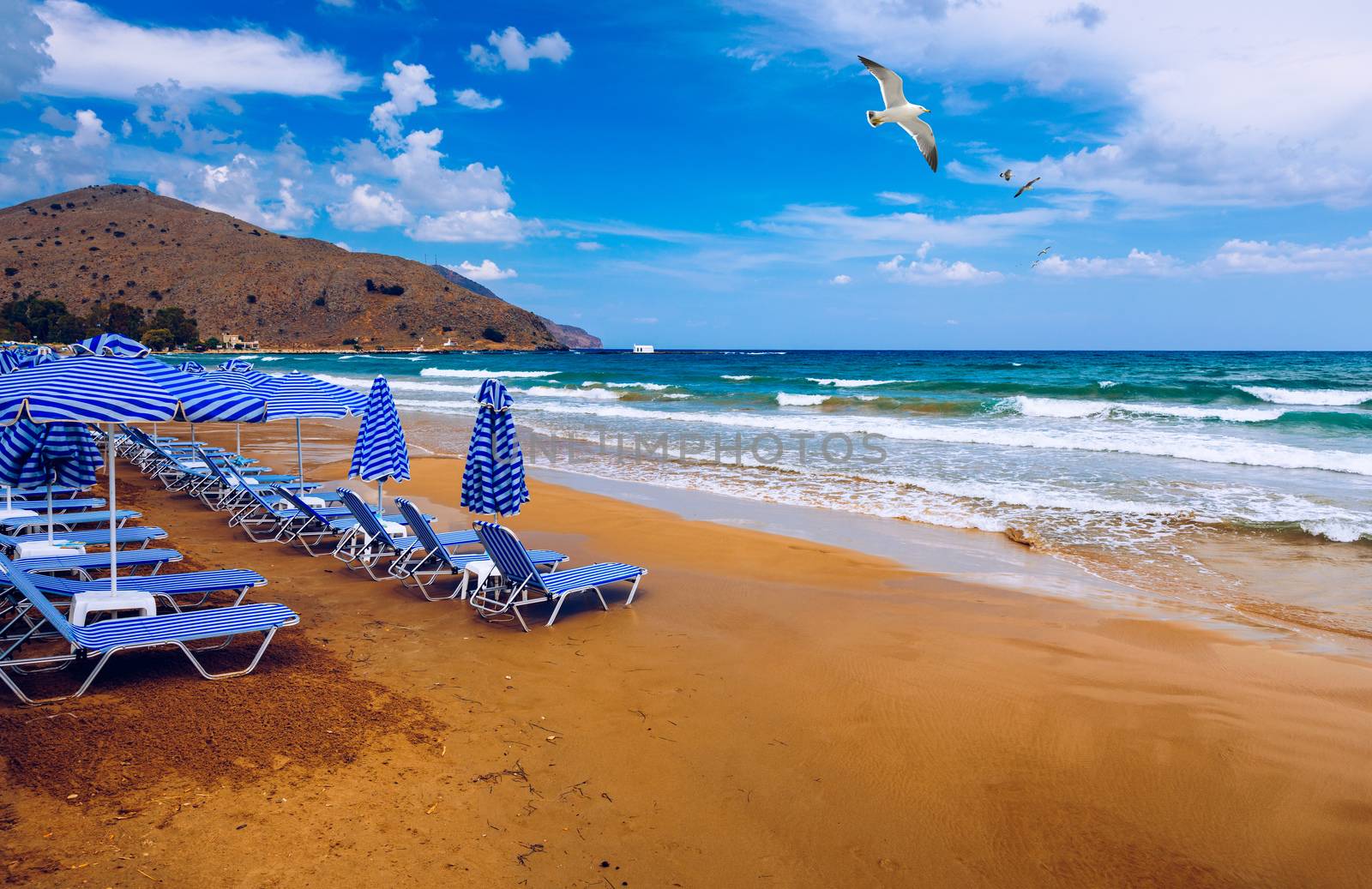 Summer vacation destination. Straw sunshades and sunbeds on the empty pebble beach with sea in the background. Vacation And Tourism Concept. Sunbeds On The Paradise Beach. Umbrellas and sunbeds.