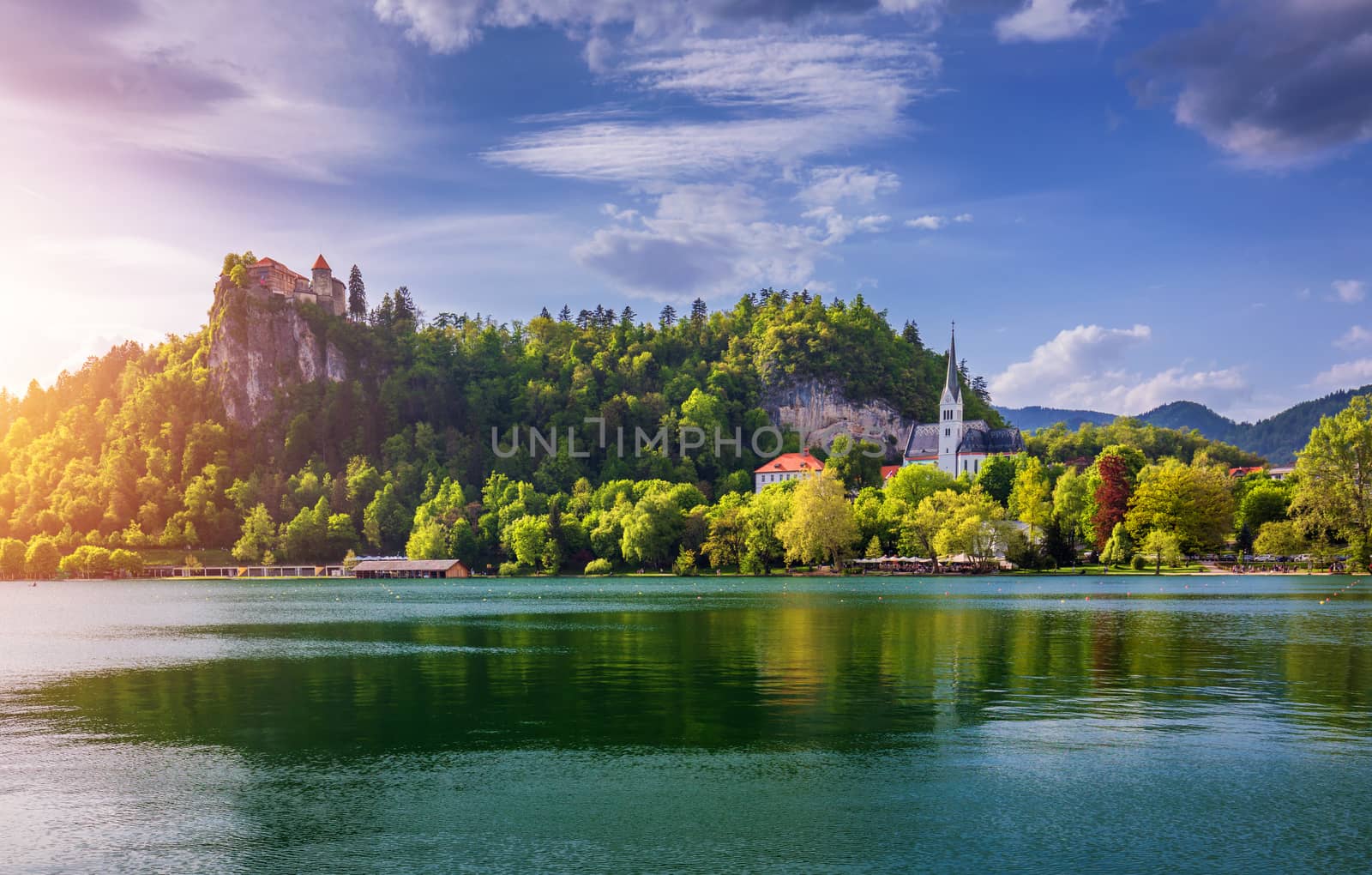 Amazing sunny scenery of Bled castle and St. Martin's Church and Bled town with reflection in the lake and the Julian Alps on background. Bled Lake, Slovenia.