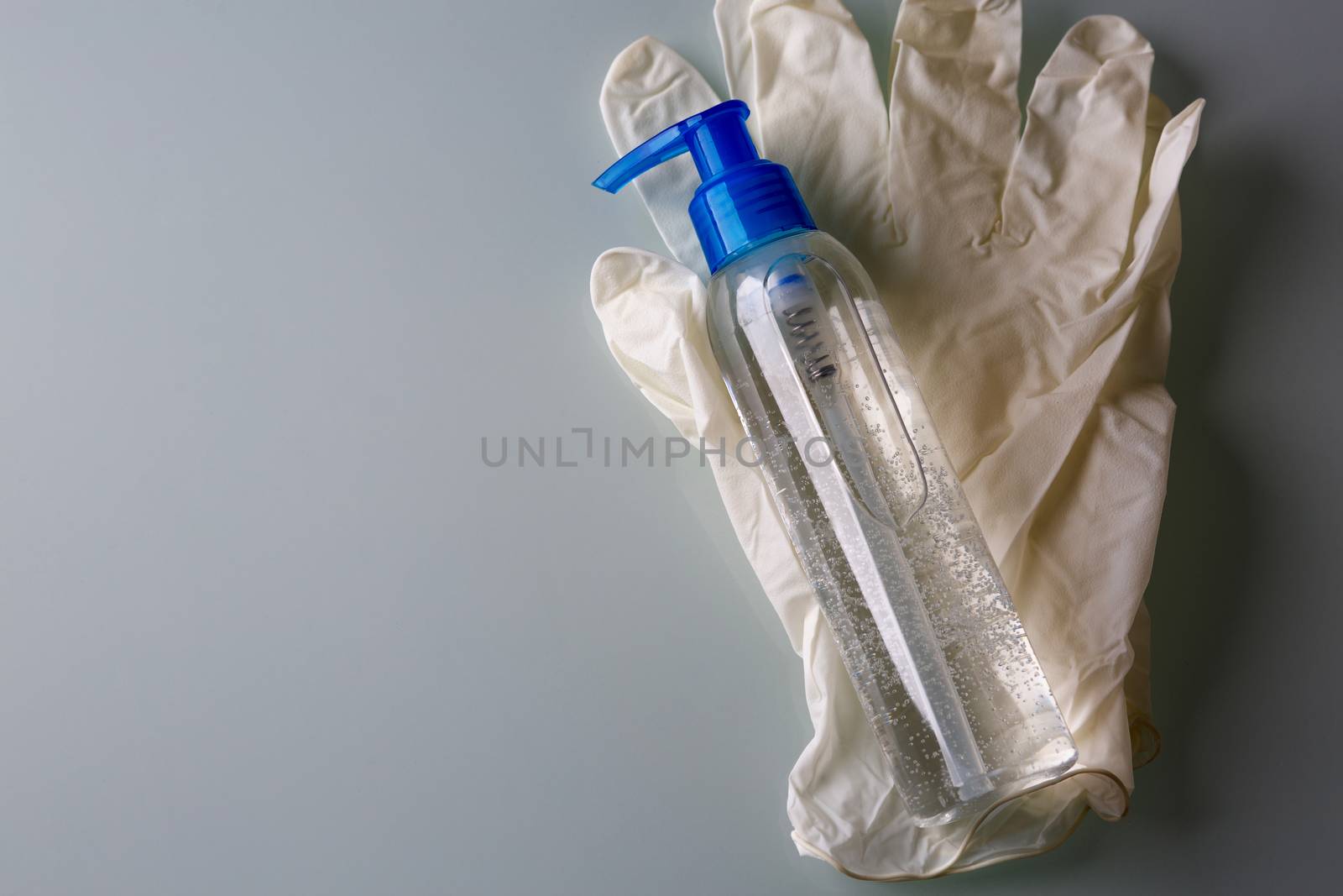 Top view of alcohol sanitizer for medical purpose with a press pump head and rubber gloves on a grey background. Empty space