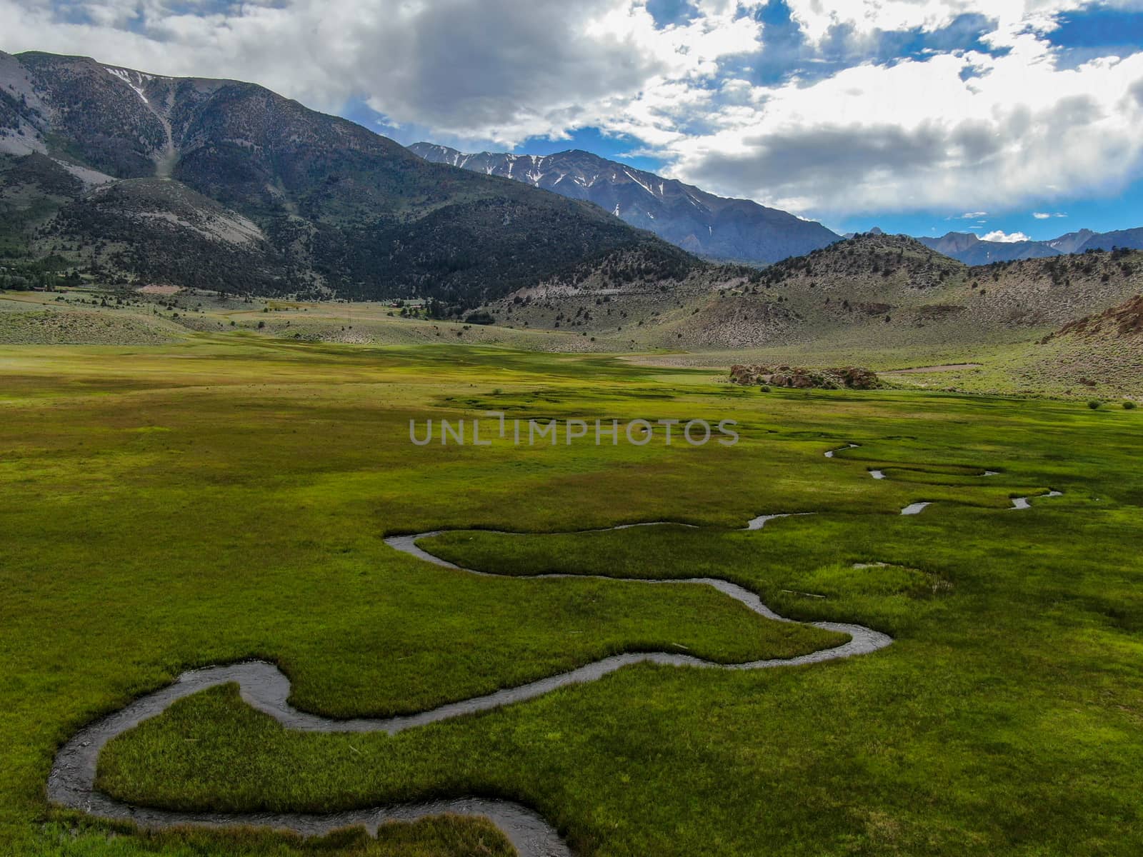 Aerial view of green land and small curve river with mountain in the background in Aspen Springs by Bonandbon