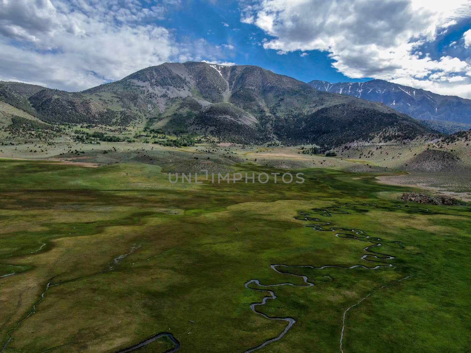 Aerial view of green land and small curve river with mountain in the background in Aspen Springs, Mono County California, USA