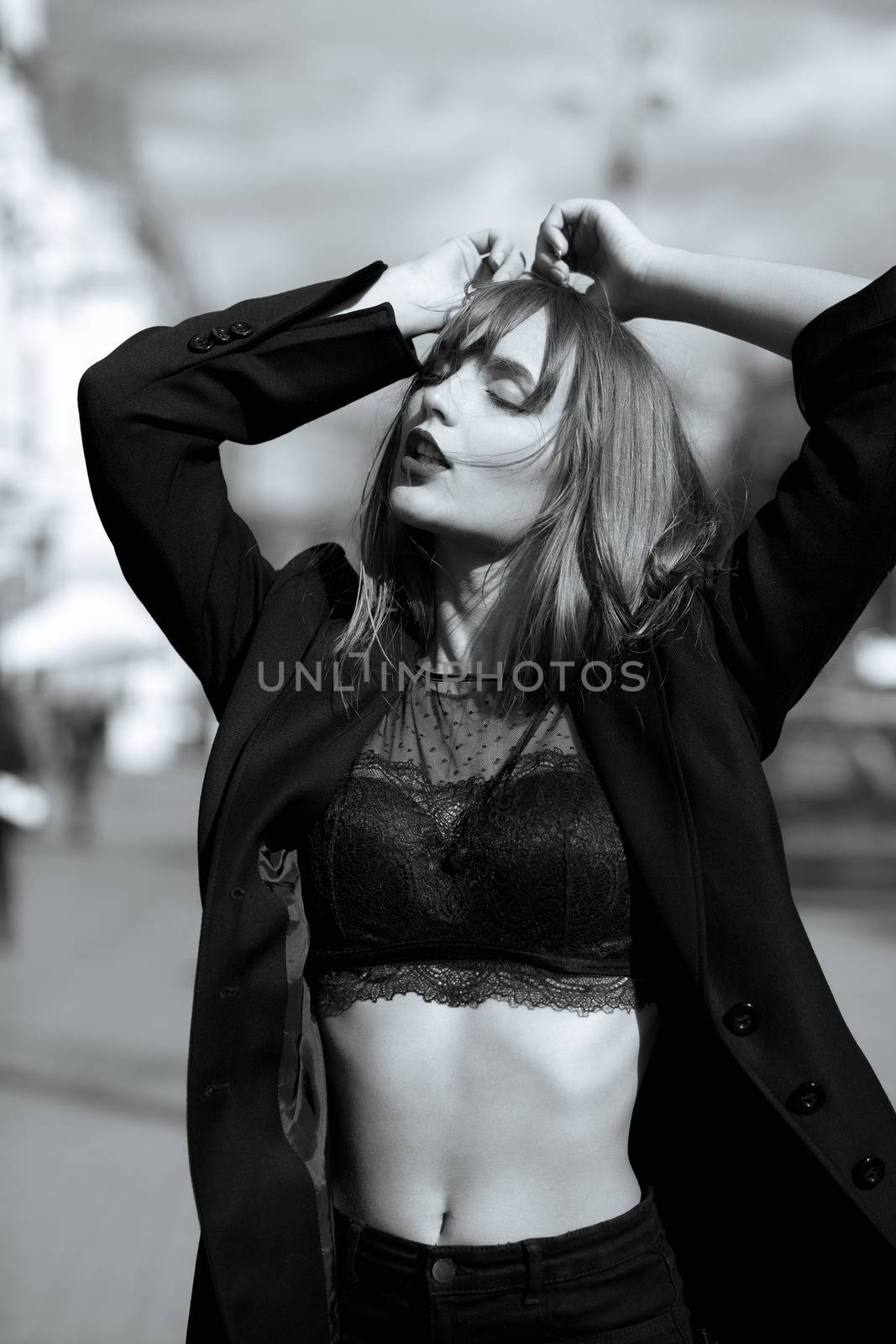 Street portrait of glamor woman with long hair wears lingerie and jacket posing at the street in Kyiv. Monochrome color