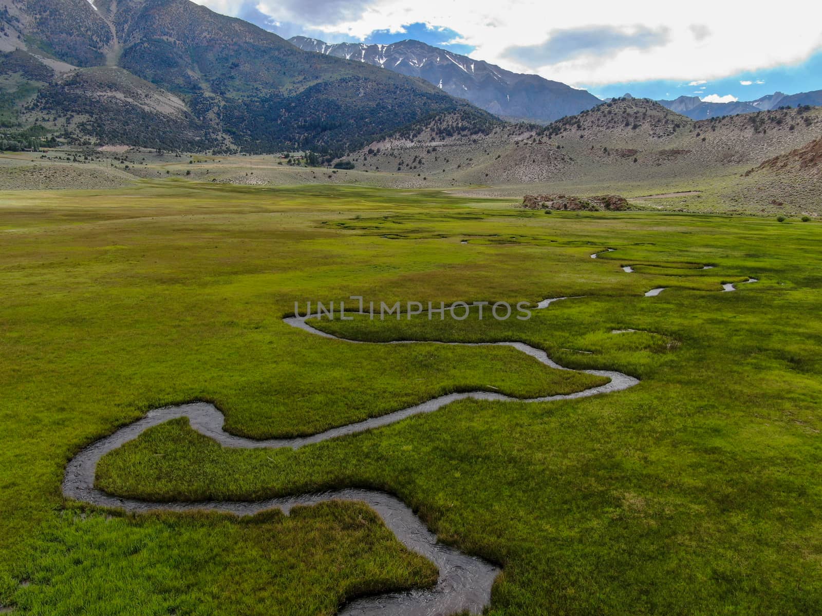 Aerial view of green land and small curve river with mountain in the background in Aspen Springs, Mono County California, USA