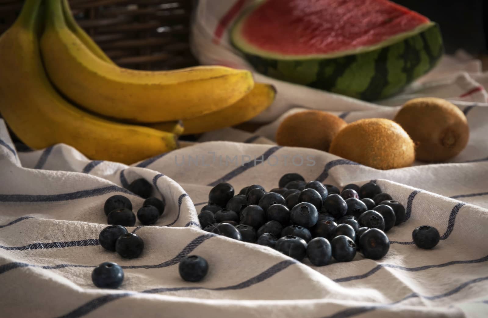 Still-life with fruits on a white tablecloth with blue lines. Blueberries, kiwis, bananas and watermelon.