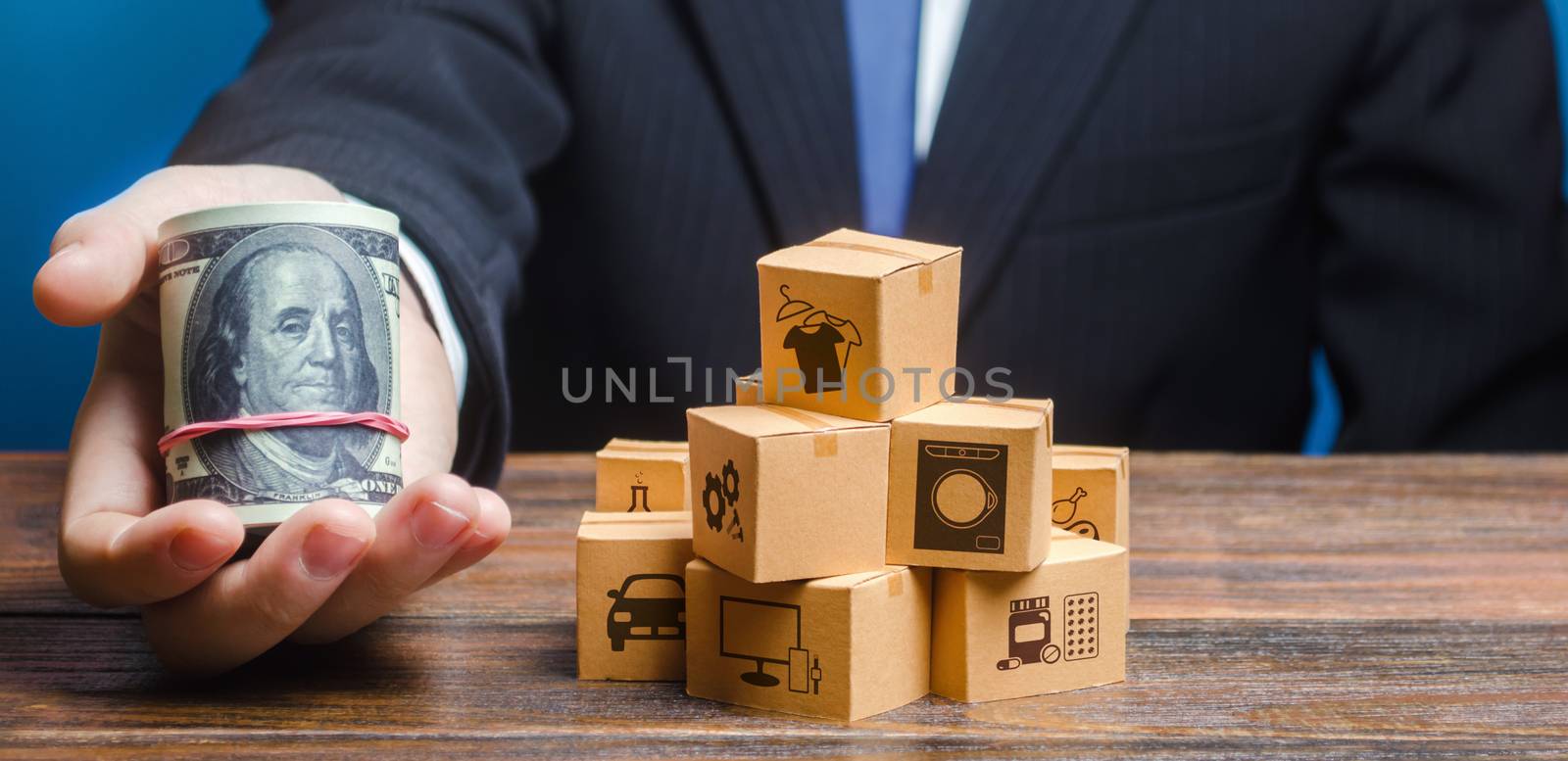 Businessman holds out a bundle of dollars near a pile of boxes. Profit, Superprofits. Investments financing in production, taxes, income revenues. Trade and exchange goods, offers for cooperation.