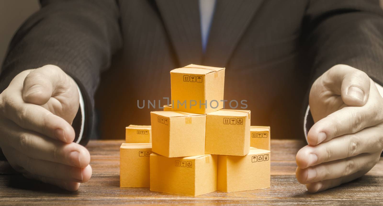 Businessman covers cardboard boxes with goods with his hands. Marketing and sales, distribution. Support for the manufacturer, attracting investment, promoting products to new markets. Brand creation