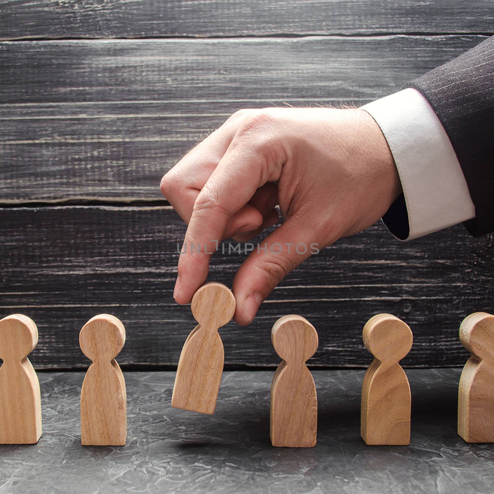 hand of a businessman takes a wooden figure of a man. The concept of search, hiring and firing workers, promotion. Business tactics and strategy, management, business management.