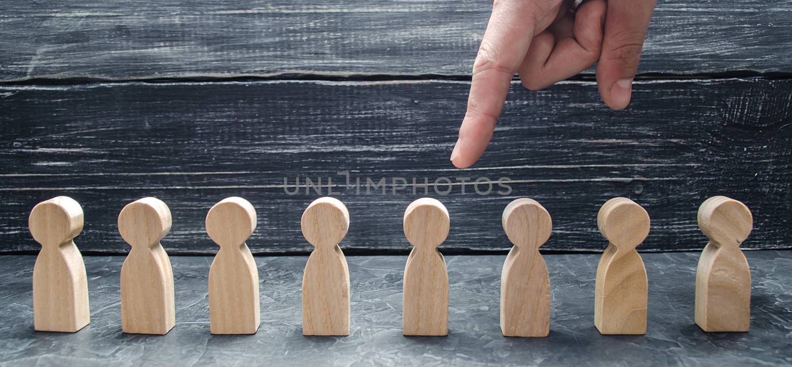 A businessman's hand points to a wooden human figure. The concept of the search for workers, management of human resources. Hiring and volnenie employees, pressure, violation of employee rights.