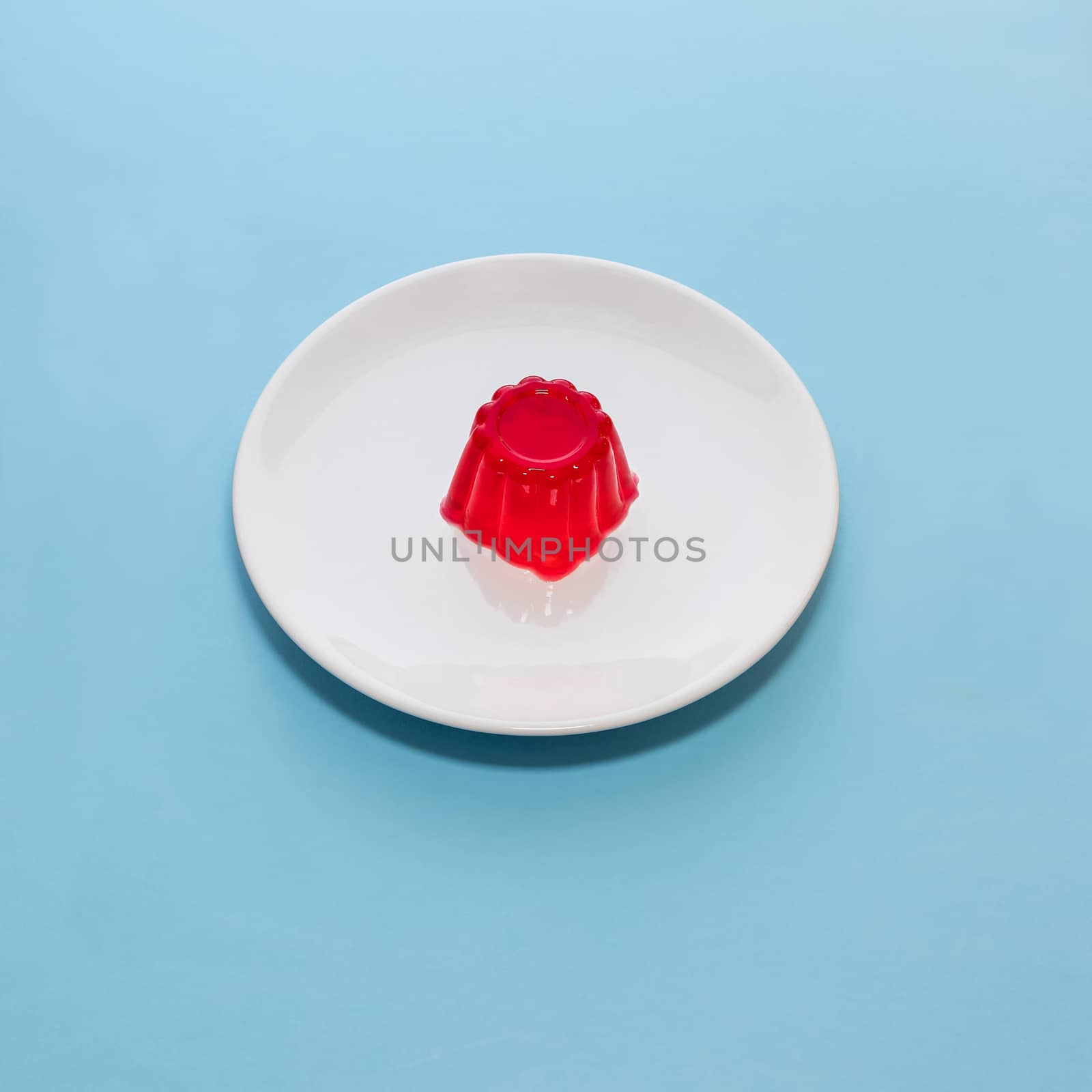 Close-up of a strawberry jelly dessert on a white plate with a light blue background