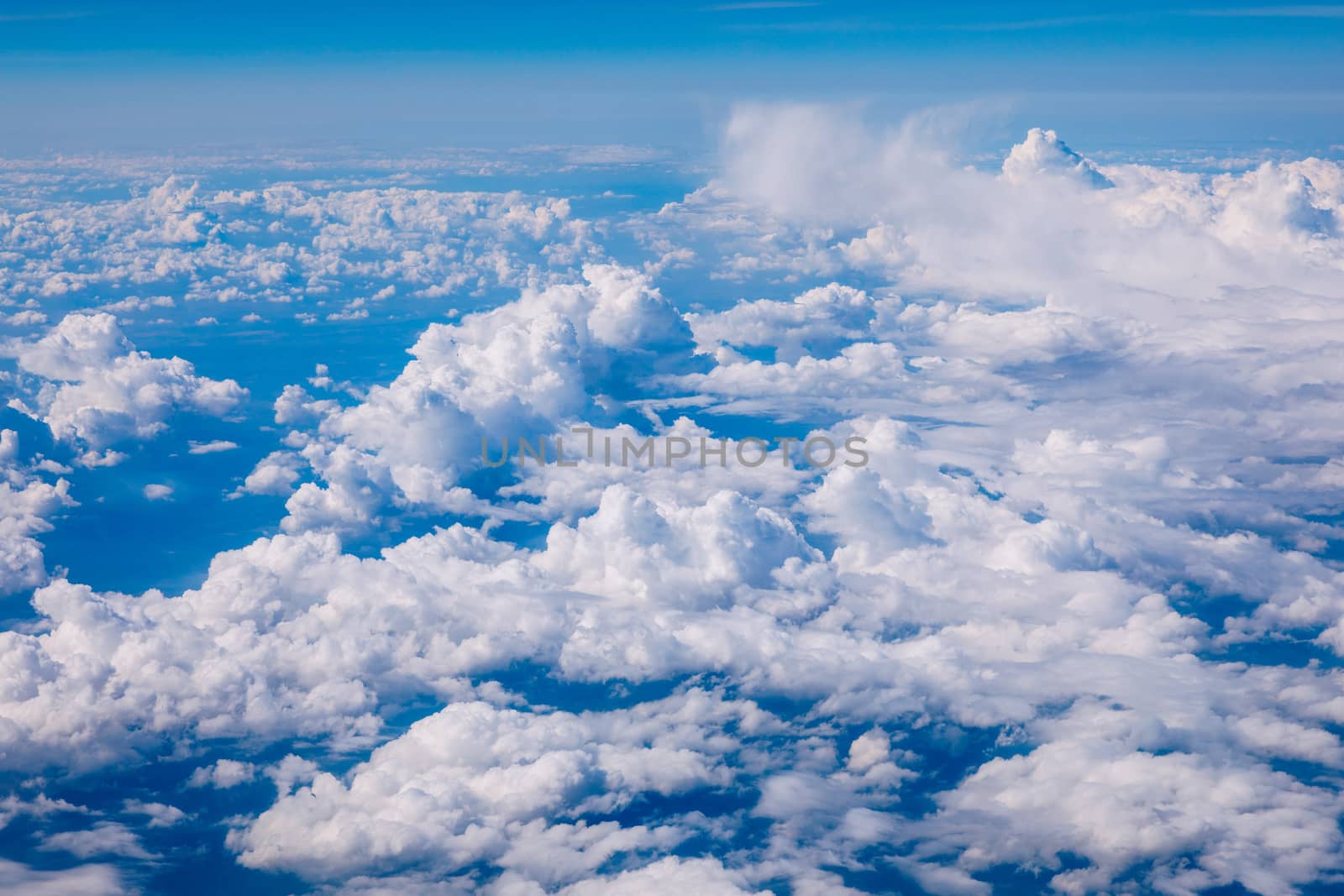 Amazing clouds and the sky as seen through the window of an aircraft. Clouds, sun, sky as seen through window of an aircraft. Bright blue sky with clouds and sunlight seen through an airplane window.