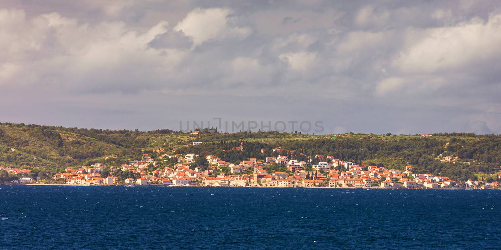 Supetar city in Brac island, Croatia. View from the sea. Picturesque scenic view on Supetar on Brac island, Croatia. Panoramic view on harbor of town Supetar from the side of sea. Brac, Croatia.