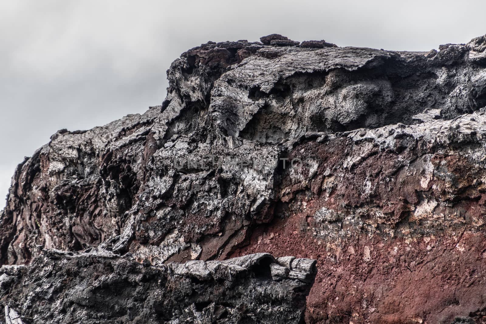 Leilani Estate, Hawaii, USA. - January 14, 2020: 2018 Kilauea volcano eruption hardened black lava field. Closeup of cliff that lost its shell exposing red rock under. Gray sky.