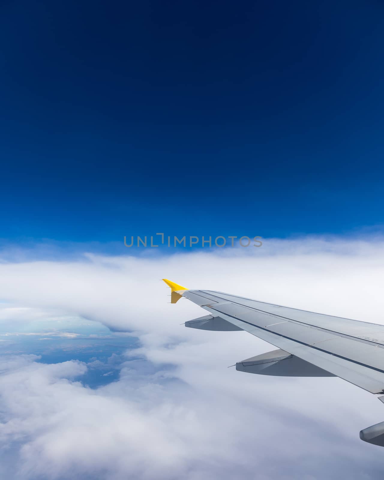 View of the wing of an airplane flying above the clouds at high altitude under a blue sky from the passenger window. In flight over Europe. View of jet airplane wing flying in blue sky over clouds.