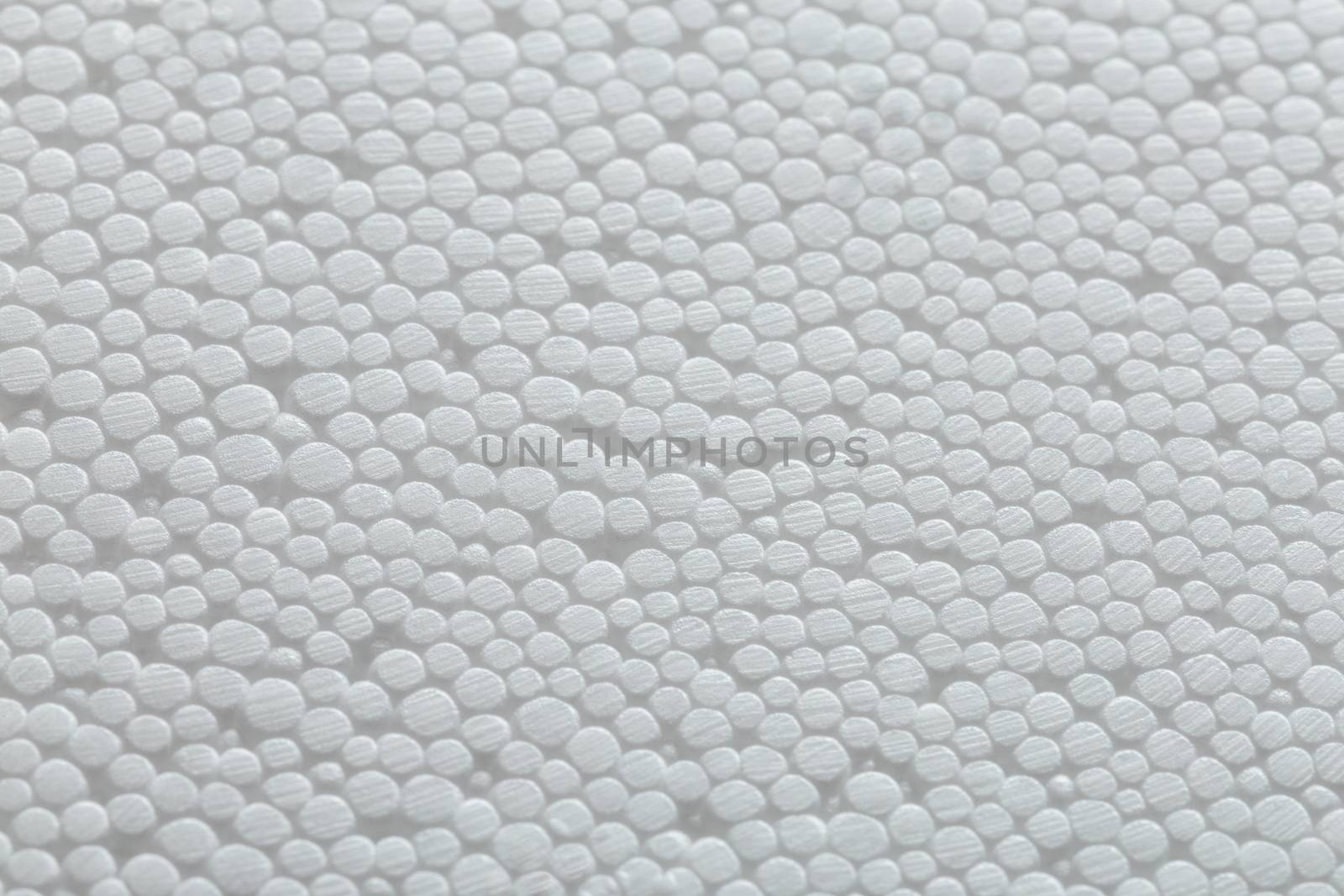 Simple close-up flat but bumpy background of white polystyrene foam or styrofoam, white on white backdrop with selective focus.