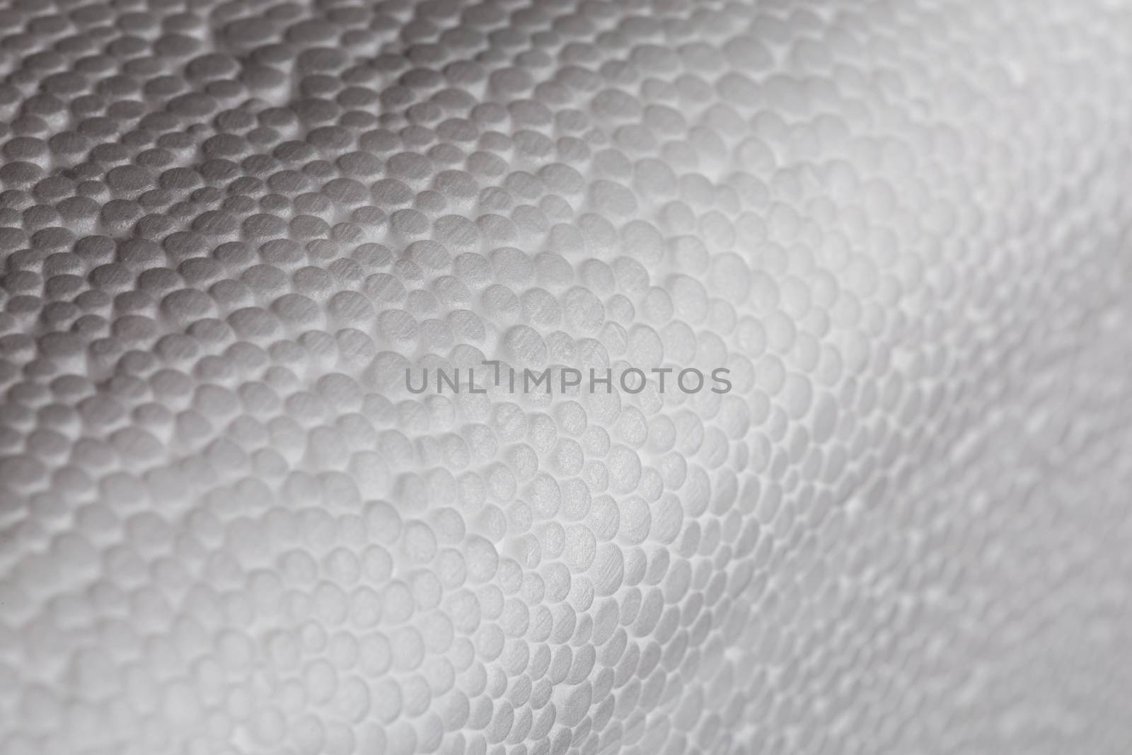 Simple close-up bumpy background of white polystyrene foam or styrofoam, white on white backdrop with selective focus.