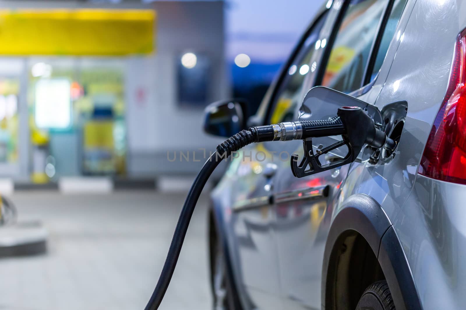 silver car refueling on night gas station - close-up with selective focus and blurry background.