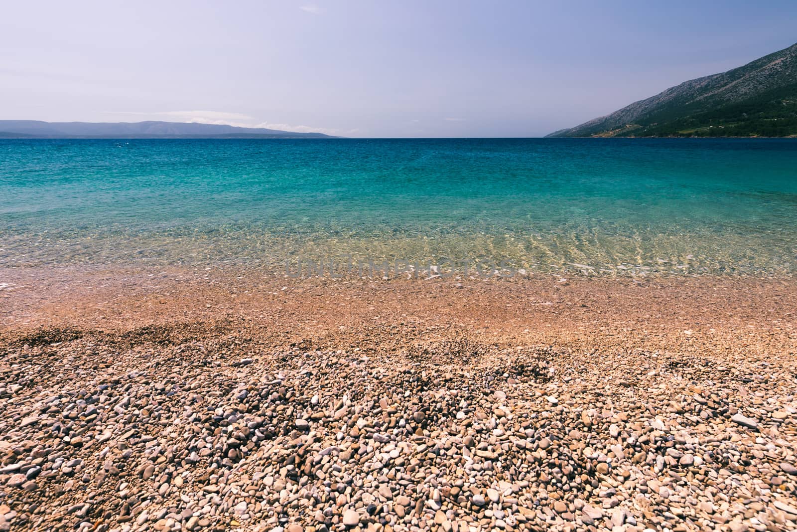 Stones under water. Sea pebbles on the beach. Sea pebbles on the beach sand with transparent water. Natural sea stones closeup. Beach smooth pebbles. Tourism and travel themed. Vacation background. 
