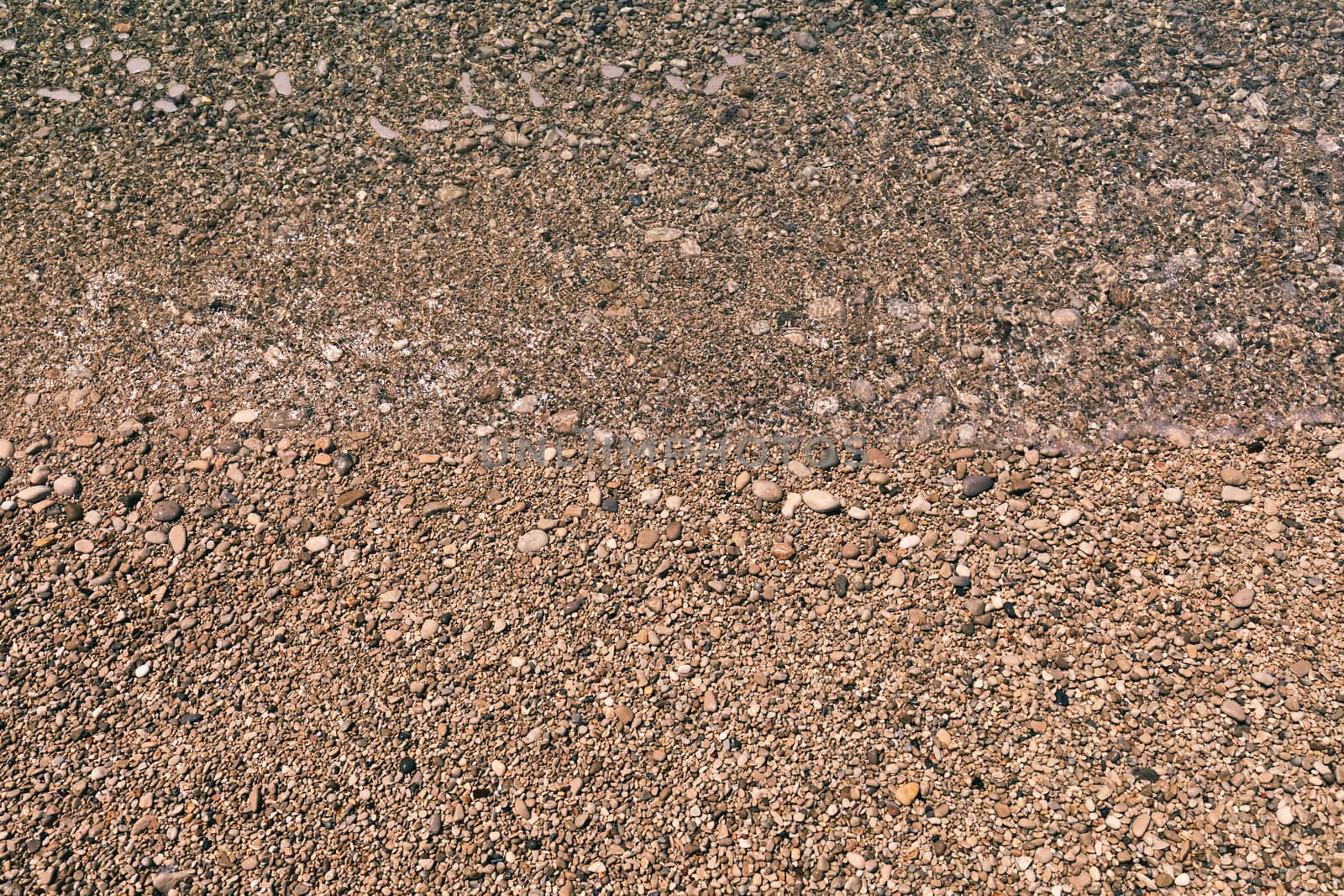 Stones under water. Sea pebbles on the beach. Sea pebbles on the beach sand with transparent water. Natural sea stones closeup. Beach smooth pebbles. Tourism and travel themed. Vacation background. 