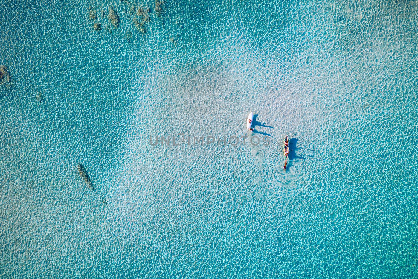 Kayaking in the sea with clear turquoise water. Kayaking, leisure activities on the ocean. Aerial drone bird's eye view of kayak cruising in tropical seascape with turquoise and sapphire clear waters.