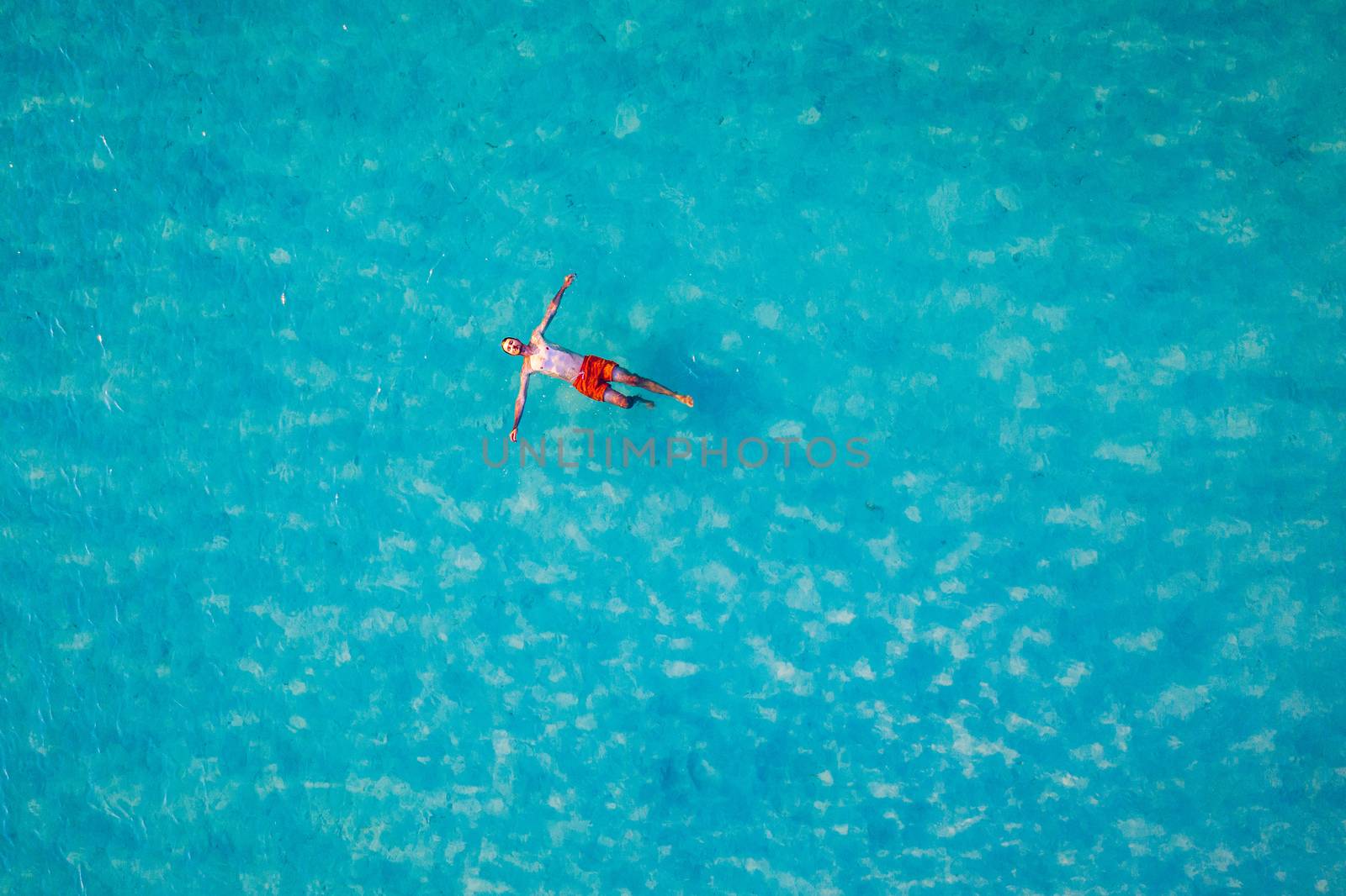 Drone view of a man floating in tropical sea water. Aerial view of young man floating on sea water enjoying sunbathing and vacations in tropical destination. People travel tourism holidays concept. 