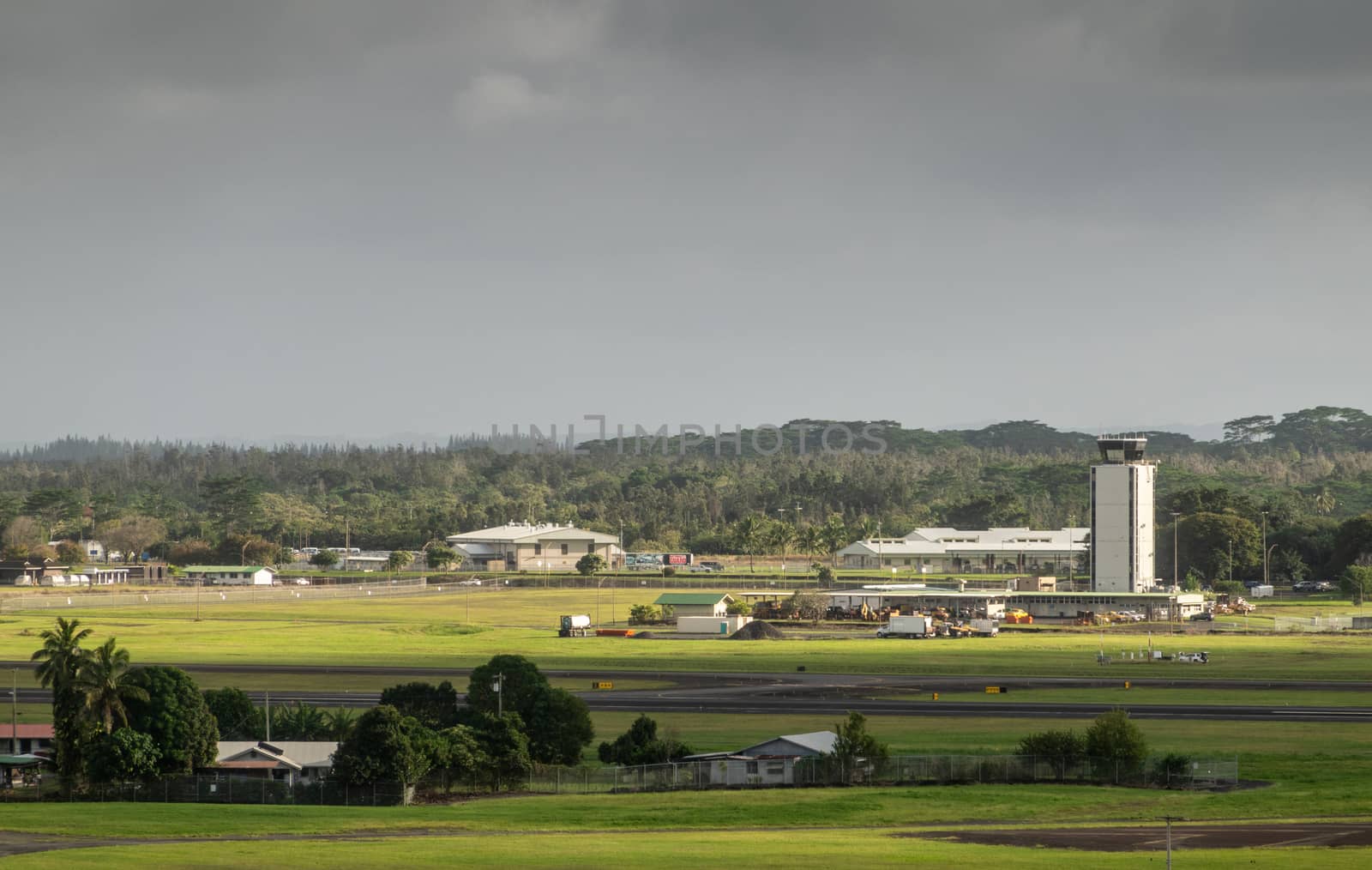 Hilo, Hawaii, USA. - January 14, 2020: Green airport with white control tower and buildings under dark rainty sky. Forest on horizon. Farm up front.