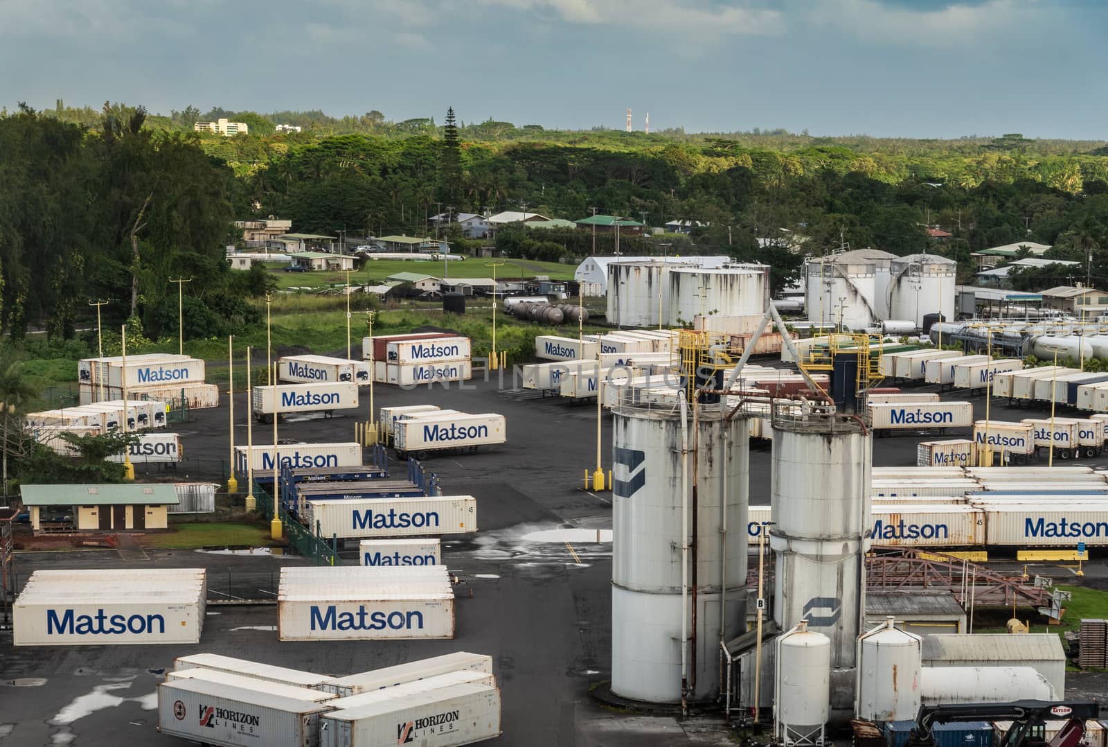 Hilo, Hawaii, USA. - January 14, 2020: Ocean port. White fuel tanks surrounded by Matson shipping containers placed on trailers. Green tree on horizon.