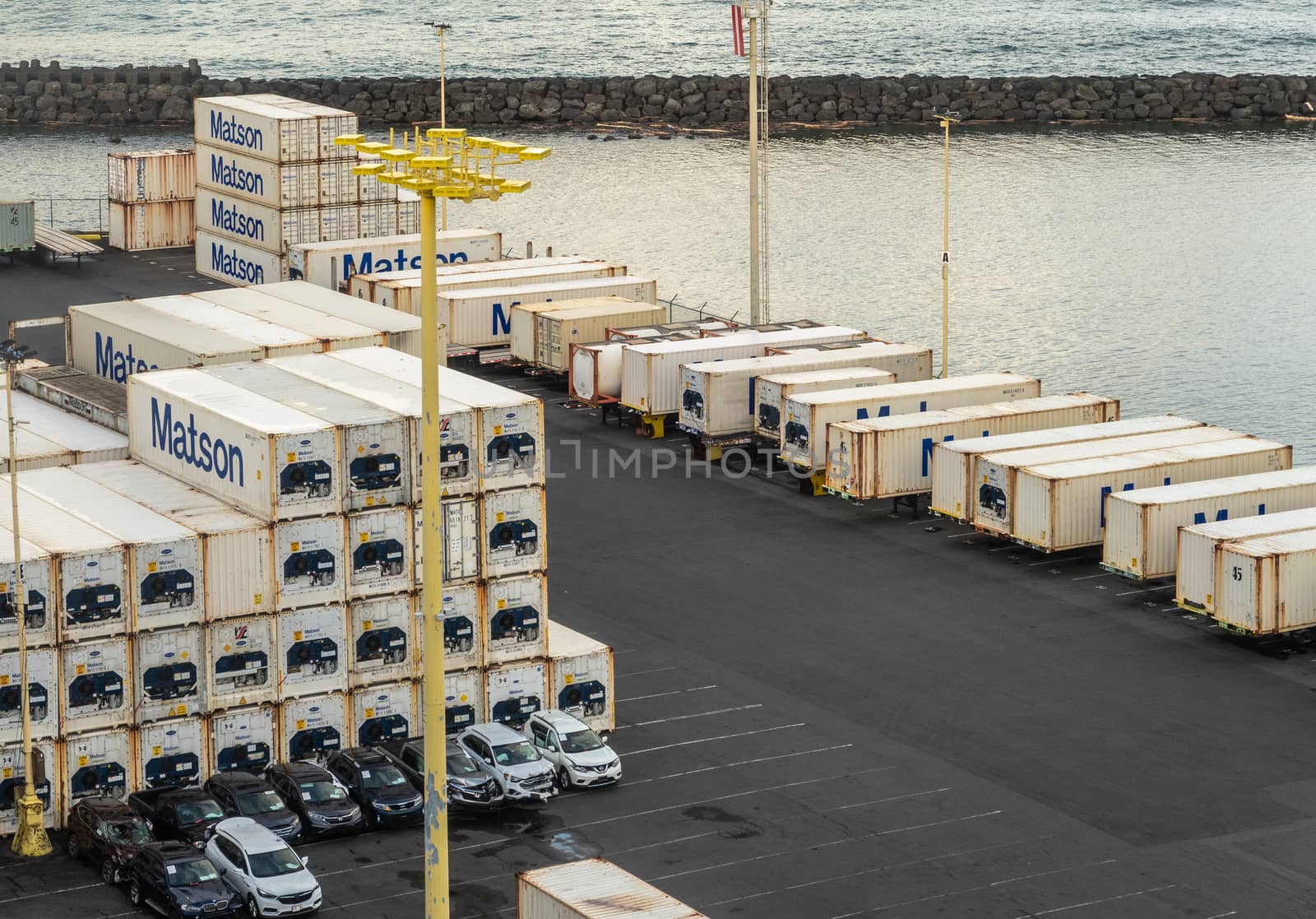 Hilo, Hawaii, USA. - January 14, 2020: Ocean port. Stacks of white and blue Matson shipping containers in quay. Breakwater separates ocean from harbor.