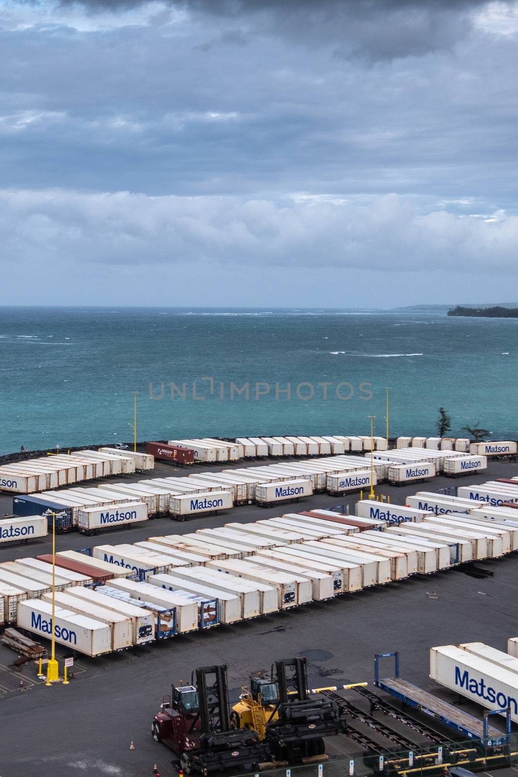 Kahului, Maui,, Hawaii, USA. - January 13, 2020: Matson shipping container yard filled with white boxes on trailers on quay bordering azure ocean under double layer cloudscape.