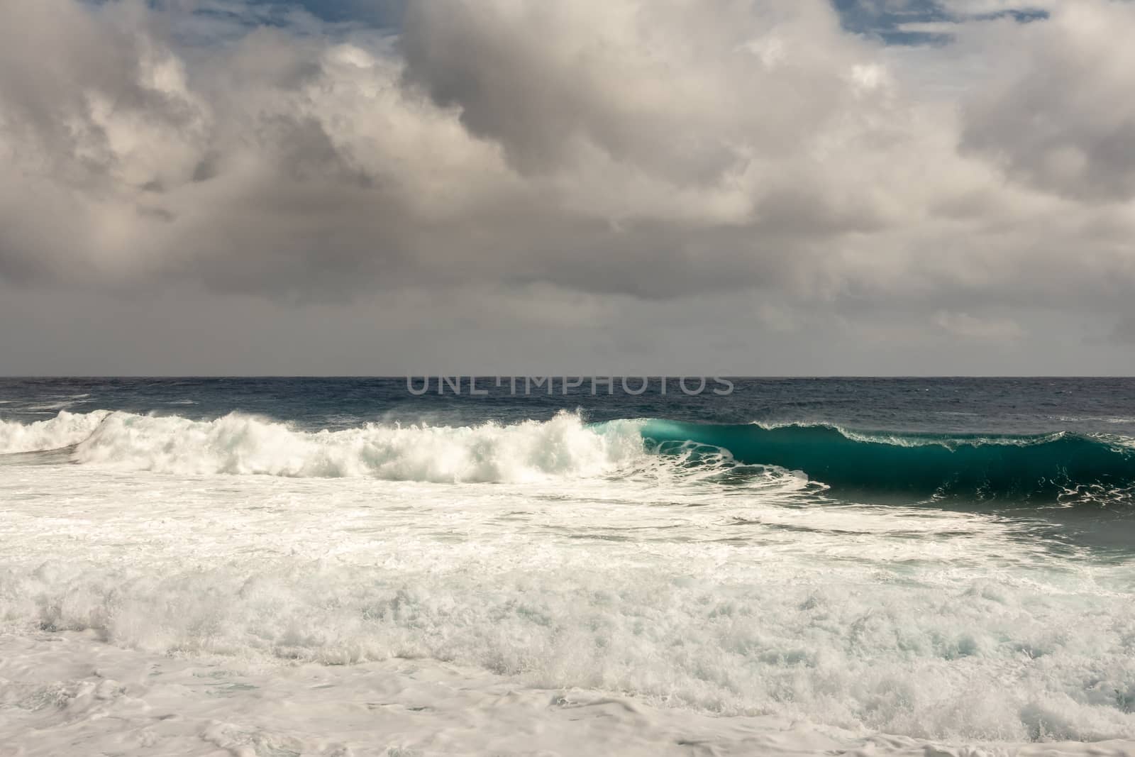 Kaimu Beach, Hawaii, USA. - January 14, 2020: Dark ocean under heavy gray cloudscape produces white surf when azure wave turns and crashes.