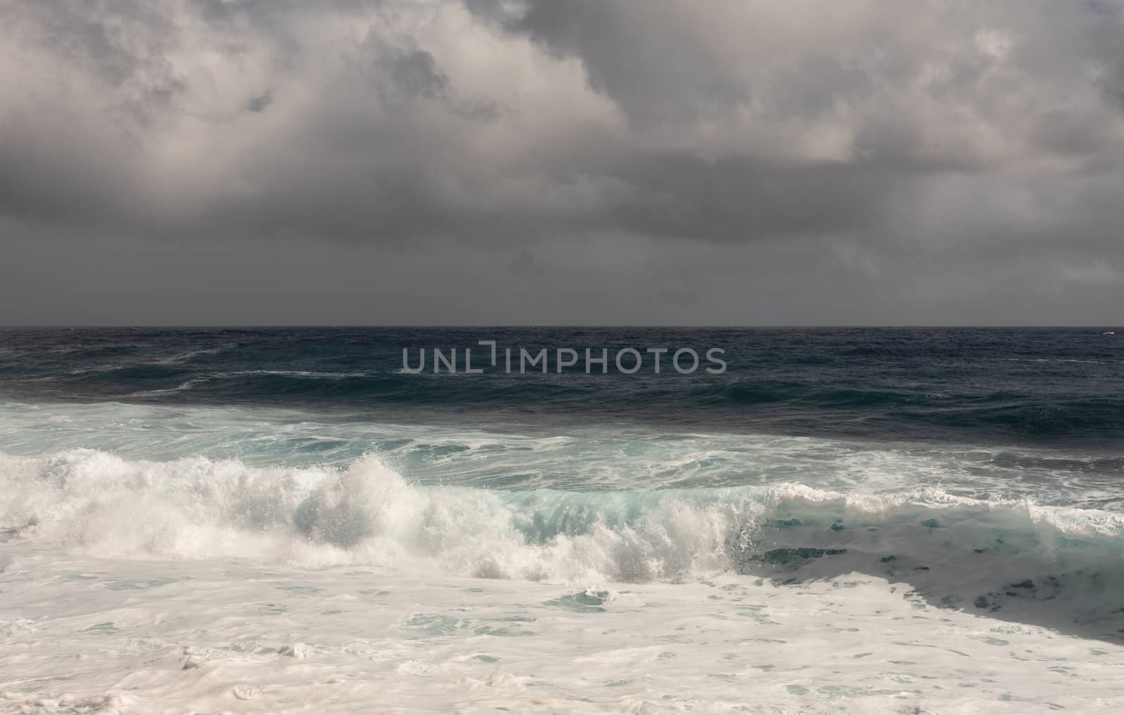 Kaimu Beach, Hawaii, USA. - January 14, 2020: Dark ocean under heavy gray rain cloudscape produces white surf when azure wave turns and crashes.