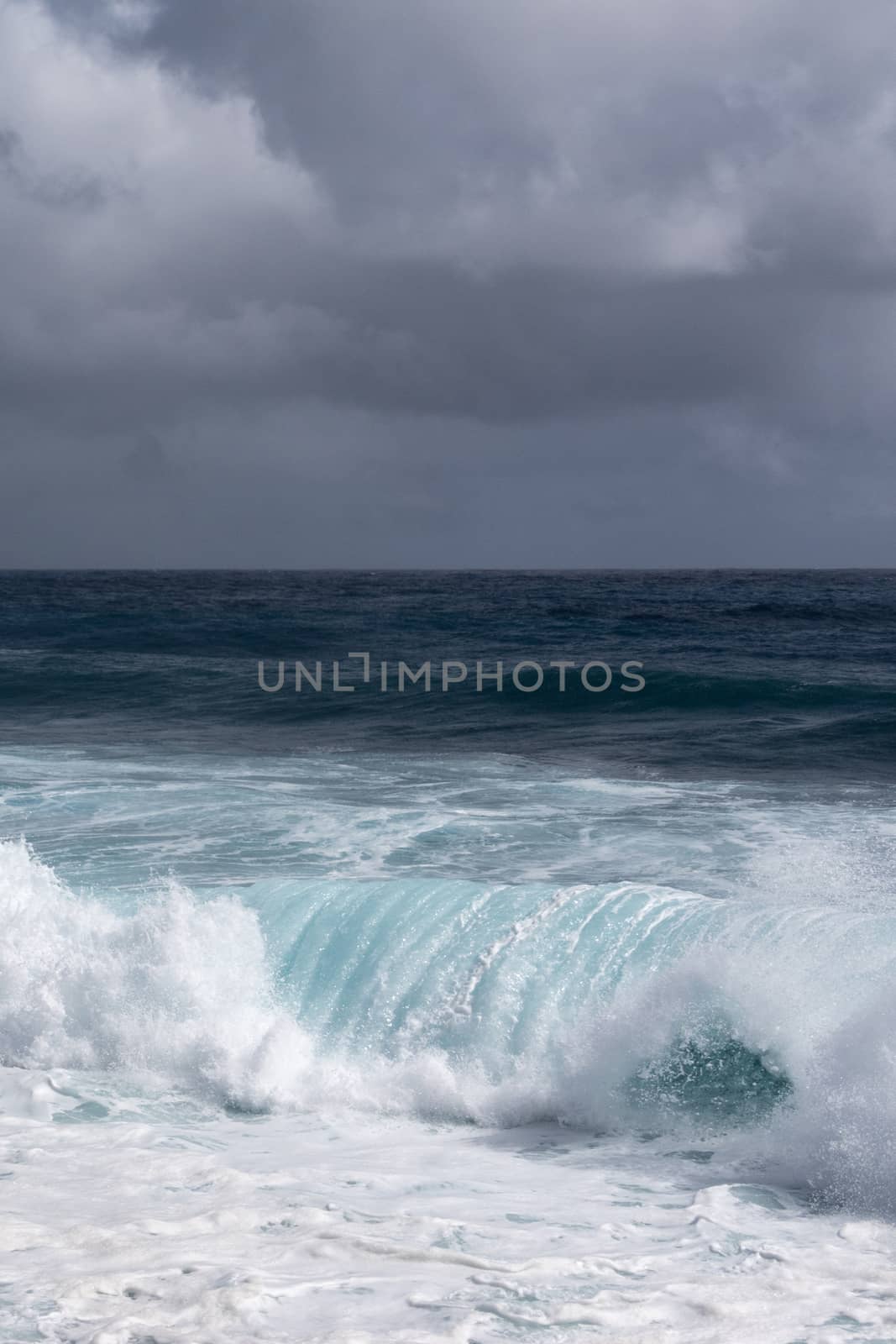 Azure wave turns into white surf under heavy cloudscape on Kaimu by Claudine