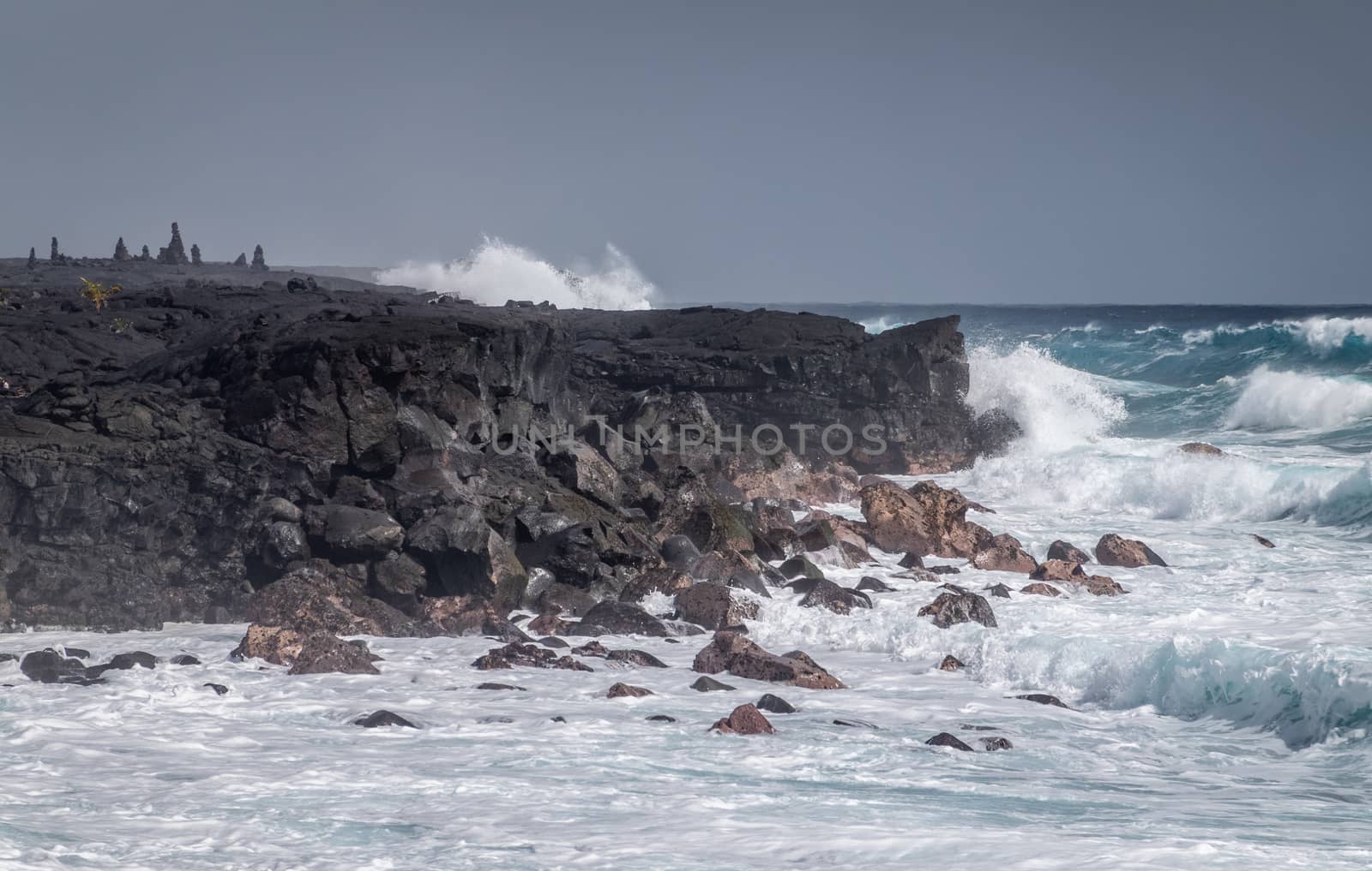 Kaimu Beach, Hawaii, USA. - January 14, 2020: Azure waves crash with white surf on black lava coastline under heavy rain gray cloudscape. 