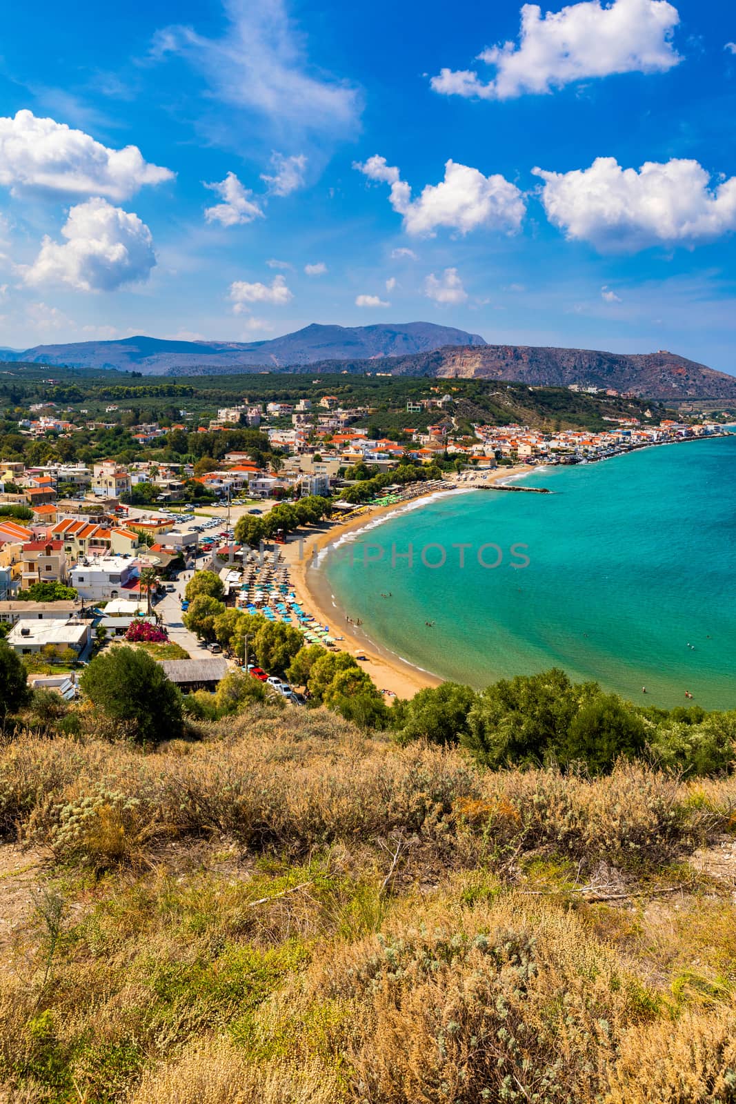 Greek holidays, beautiful Kalyves village with turquoise sea in Crete island, Greece. View of Kalyves beach, Crete. Tourists relaxing on the beach and views to the mountains, Kalyves, Crete, Greece