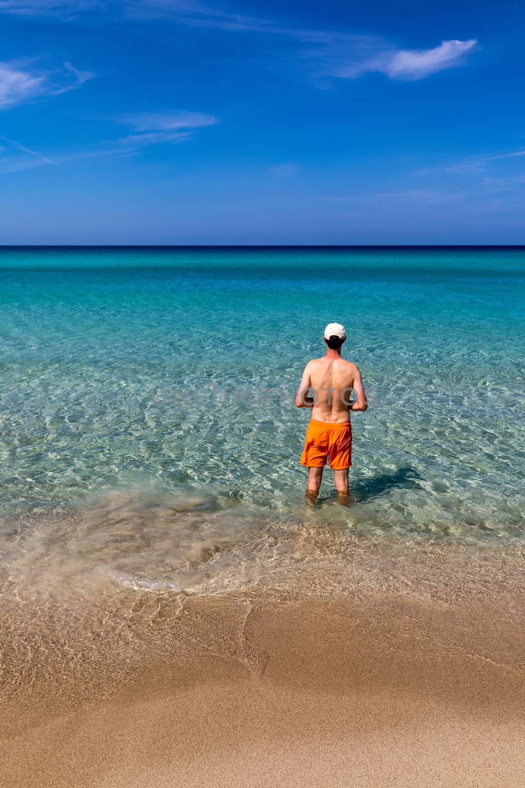 Man in the water at the sea concept of a happy holiday and freedom. Young man in the sea water on beach summer vacation, guy standing back seaside, blue sea water, holiday travel concept.