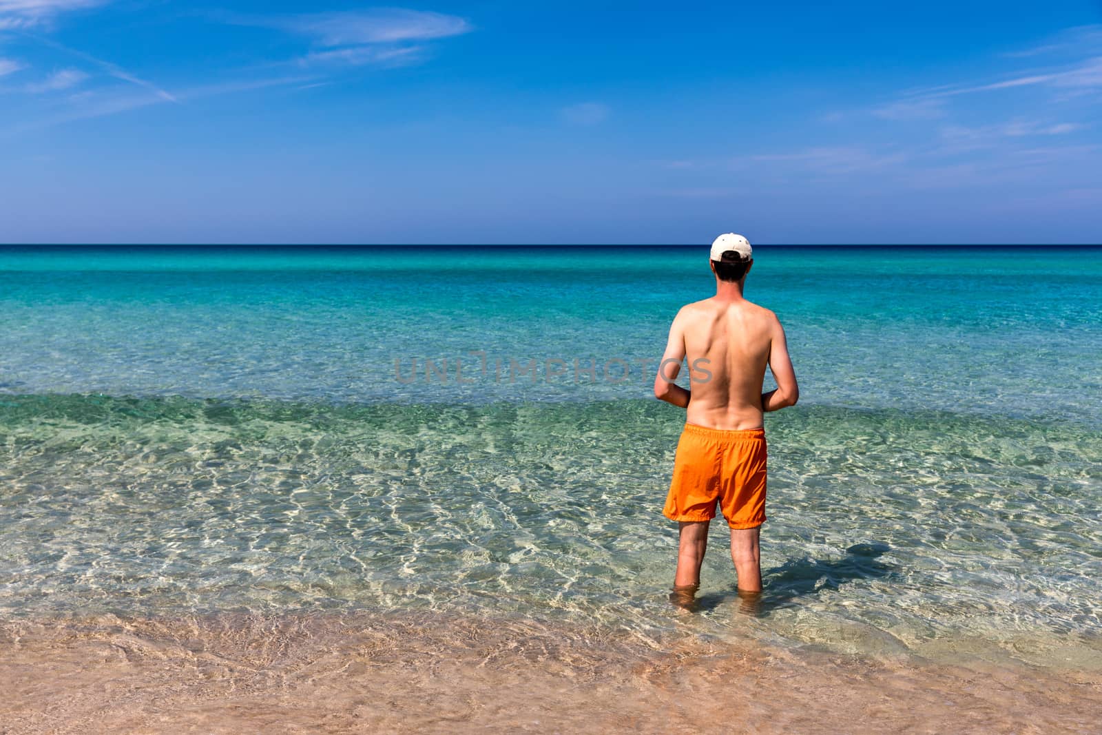 Man in the water at the sea concept of a happy holiday and freedom. Young man in the sea water on beach summer vacation, guy standing back seaside, blue sea water, holiday travel concept.