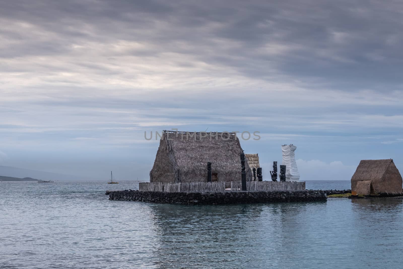 Kona, Hawaii, USA. - January 15, 2020: Kamakahonu Historic landmark. Aboriginal brown palm tree leaves huts on platform in harbor under cloudscape and floating on dark water.