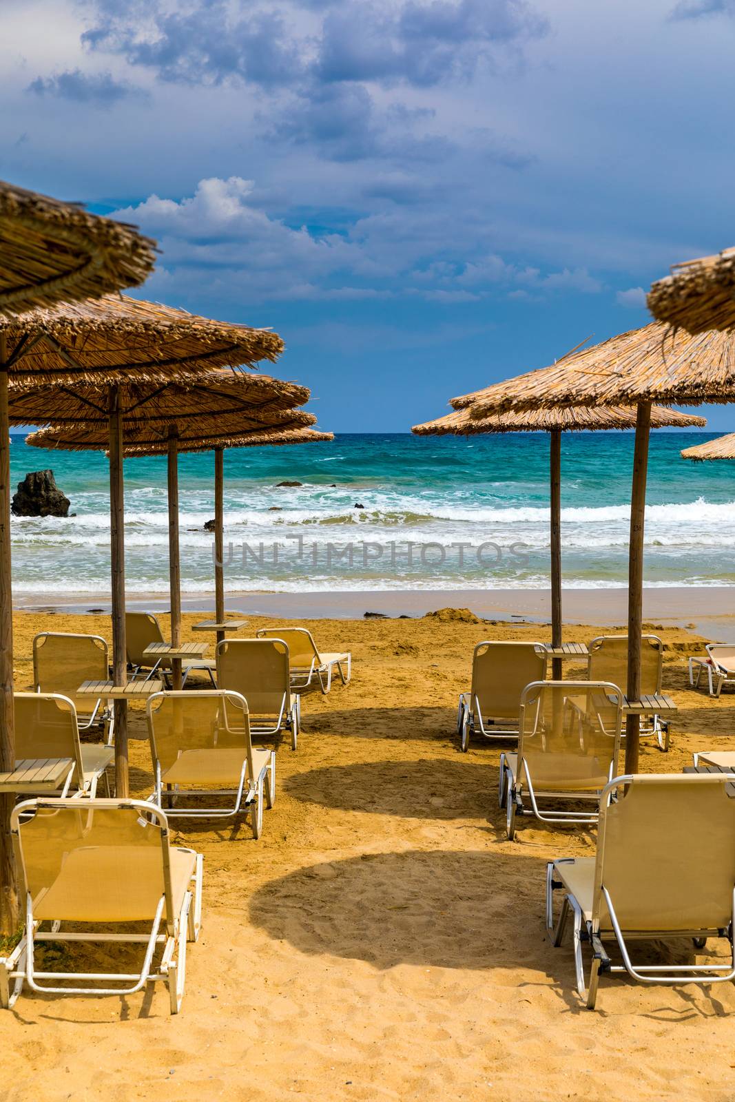 Summer vacation destination. Straw sunshades and sunbeds on the empty pebble beach with sea in the background. Vacation And Tourism Concept. Sunbeds On The Paradise Beach. Umbrellas and sunbeds.