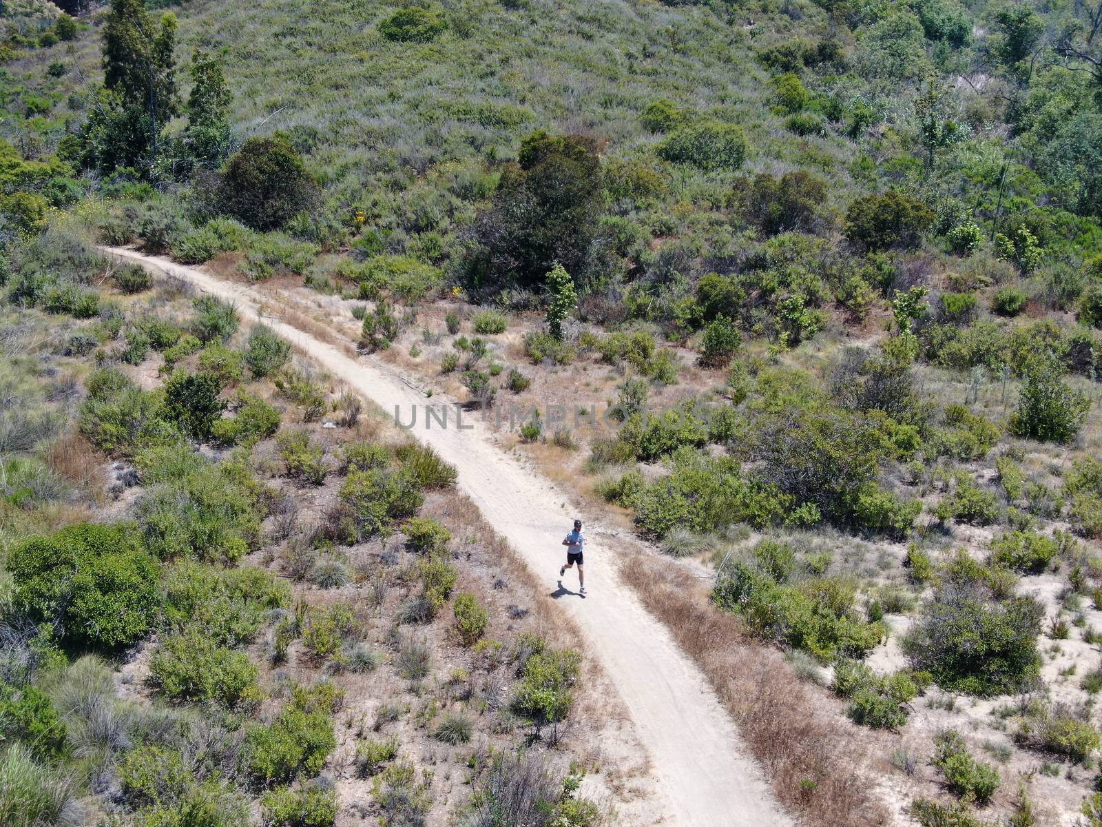Aerial view of running man mountain bike in a small singletrack dusty trail in the valley California, USA