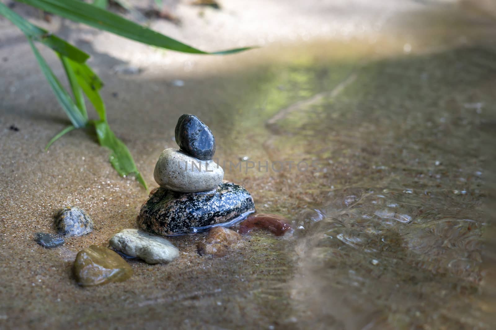 Small stack of pebbles or stones in a stream carefully balanced on each other with rippling sunlit water flowing past