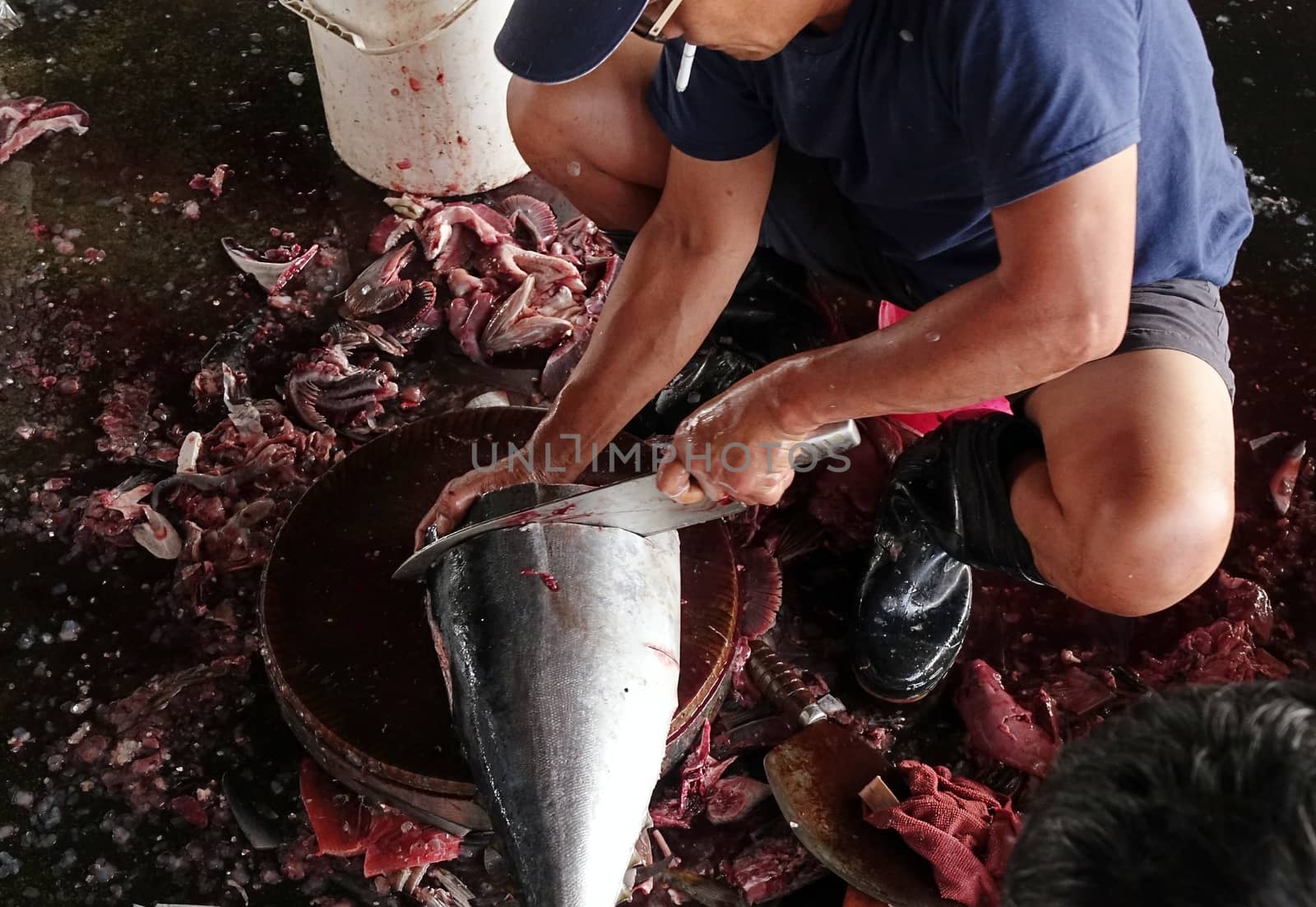 KAOHSIUNG, TAIWAN -- MAY 9, 2015: A local fishmonger cleans and slices a large tuna fish at the Sinda fishmarket.