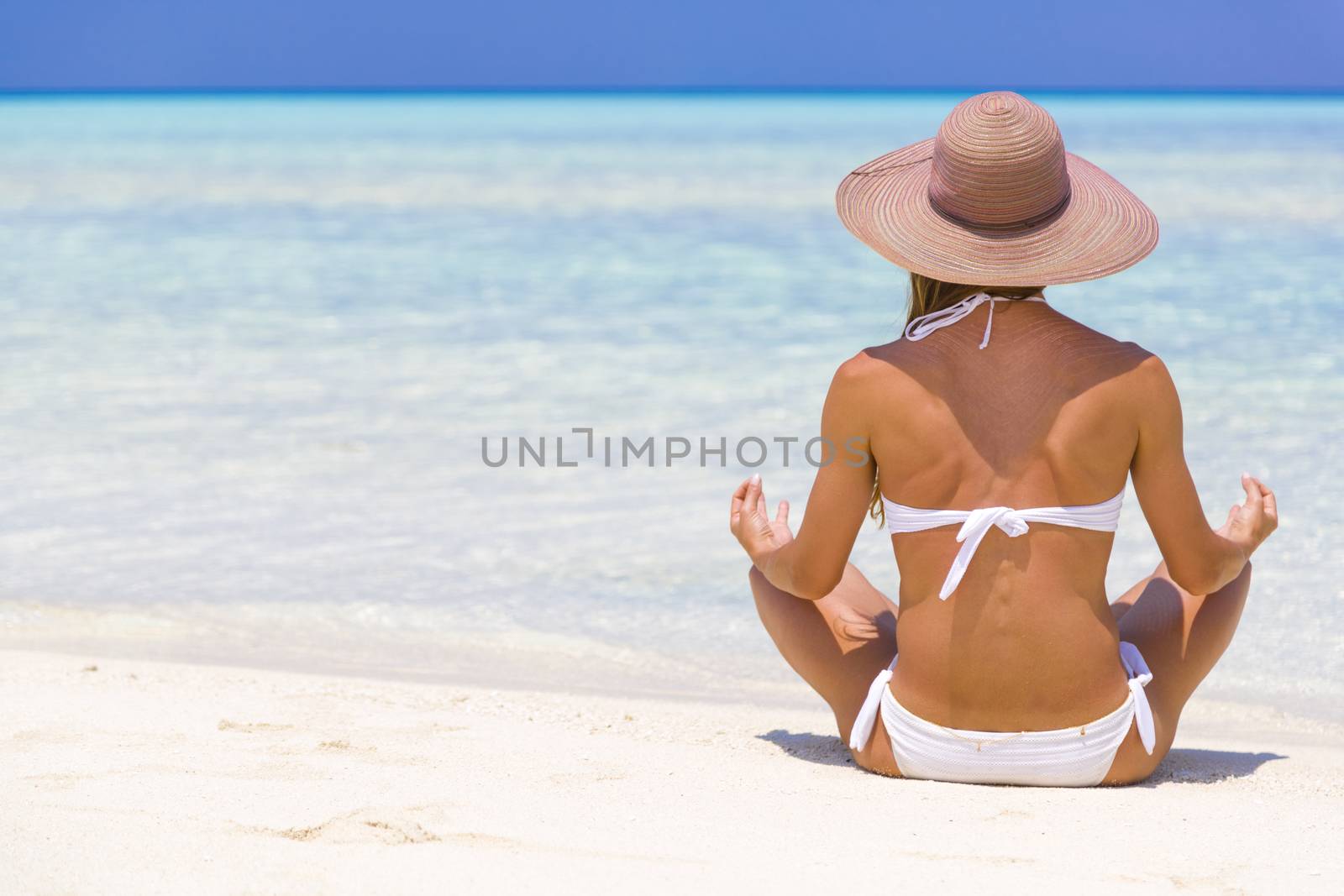 Young lady sitting on the shore in Maldives with straw hat meditating.