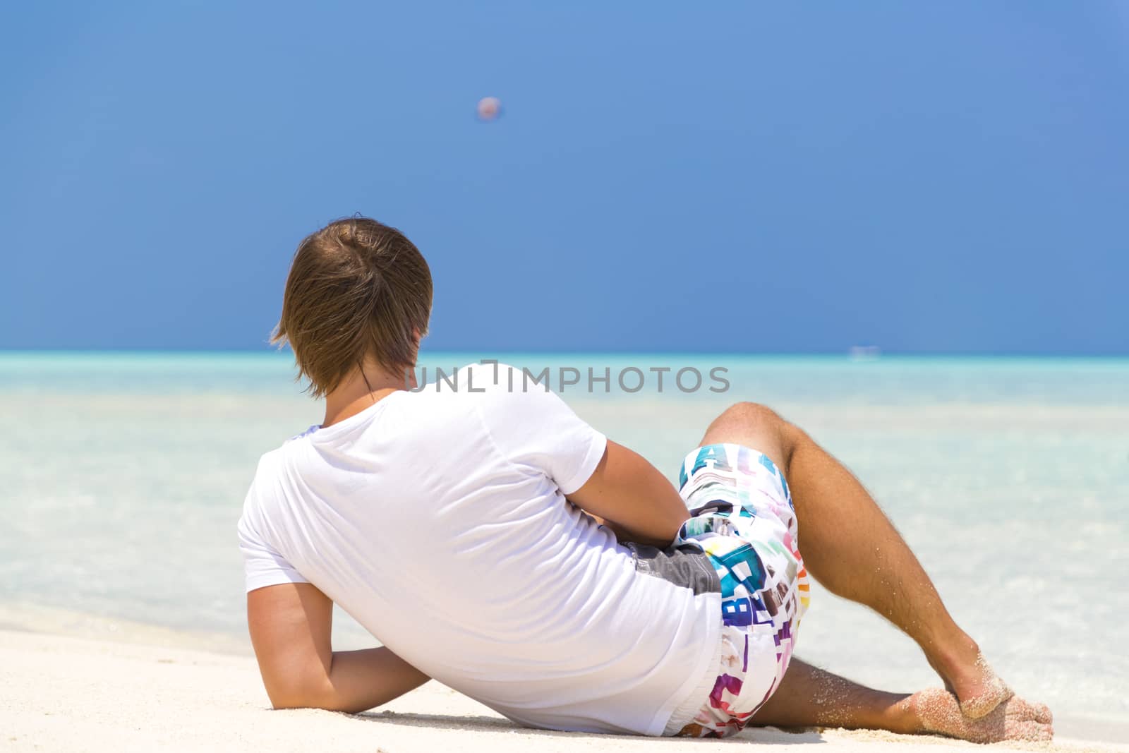 Man relaxing in the beach while he is looking at the horizon.