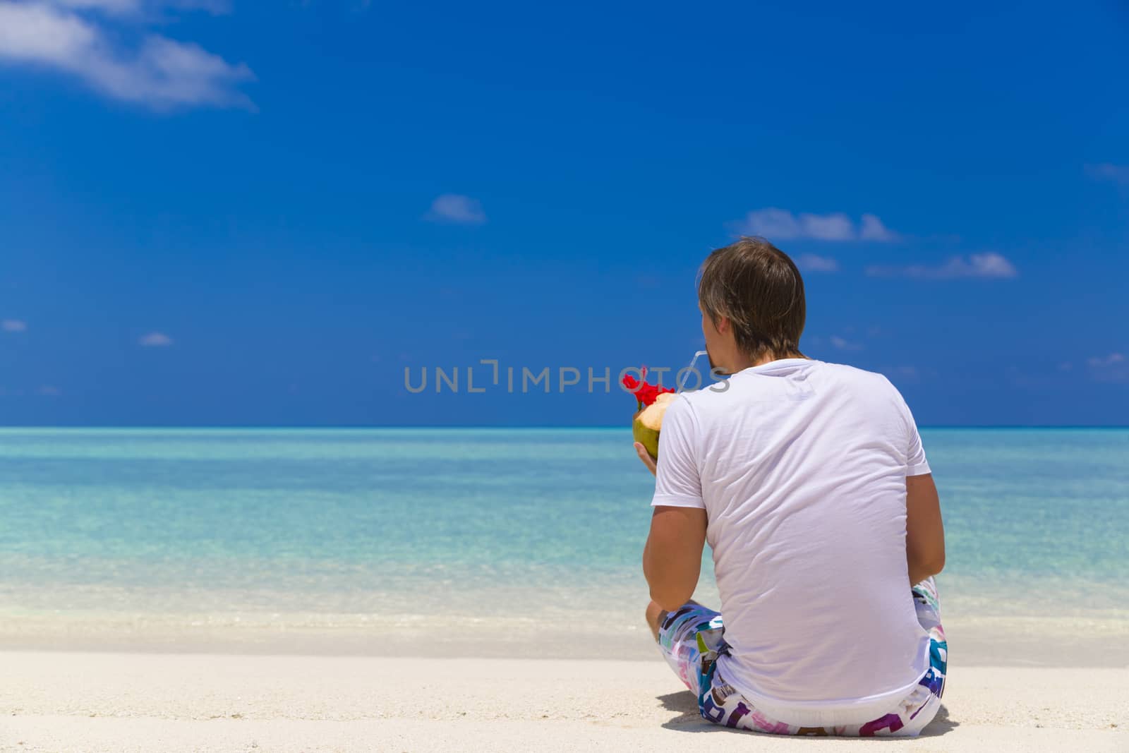 Man seated in the beach while he drinks coconut  water and relax.